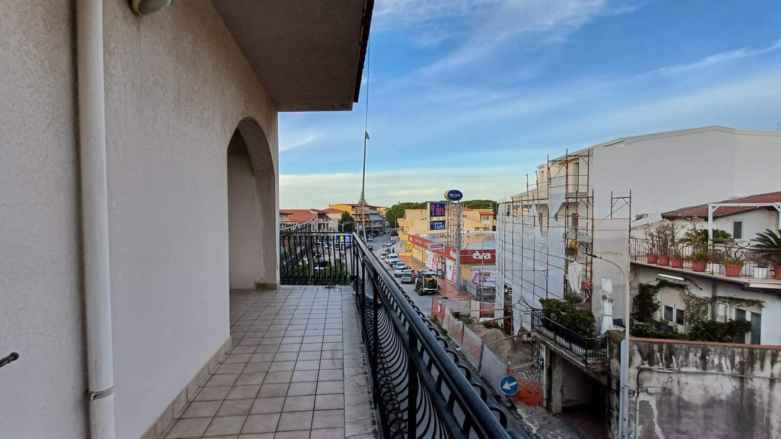 Vista panoramica dal balcone di un appartamento in zona urbana, con costruzioni in corso e negozi commerciali, perfetto per chi cerca immobili con vista città e opportunità di investimento immobiliare.