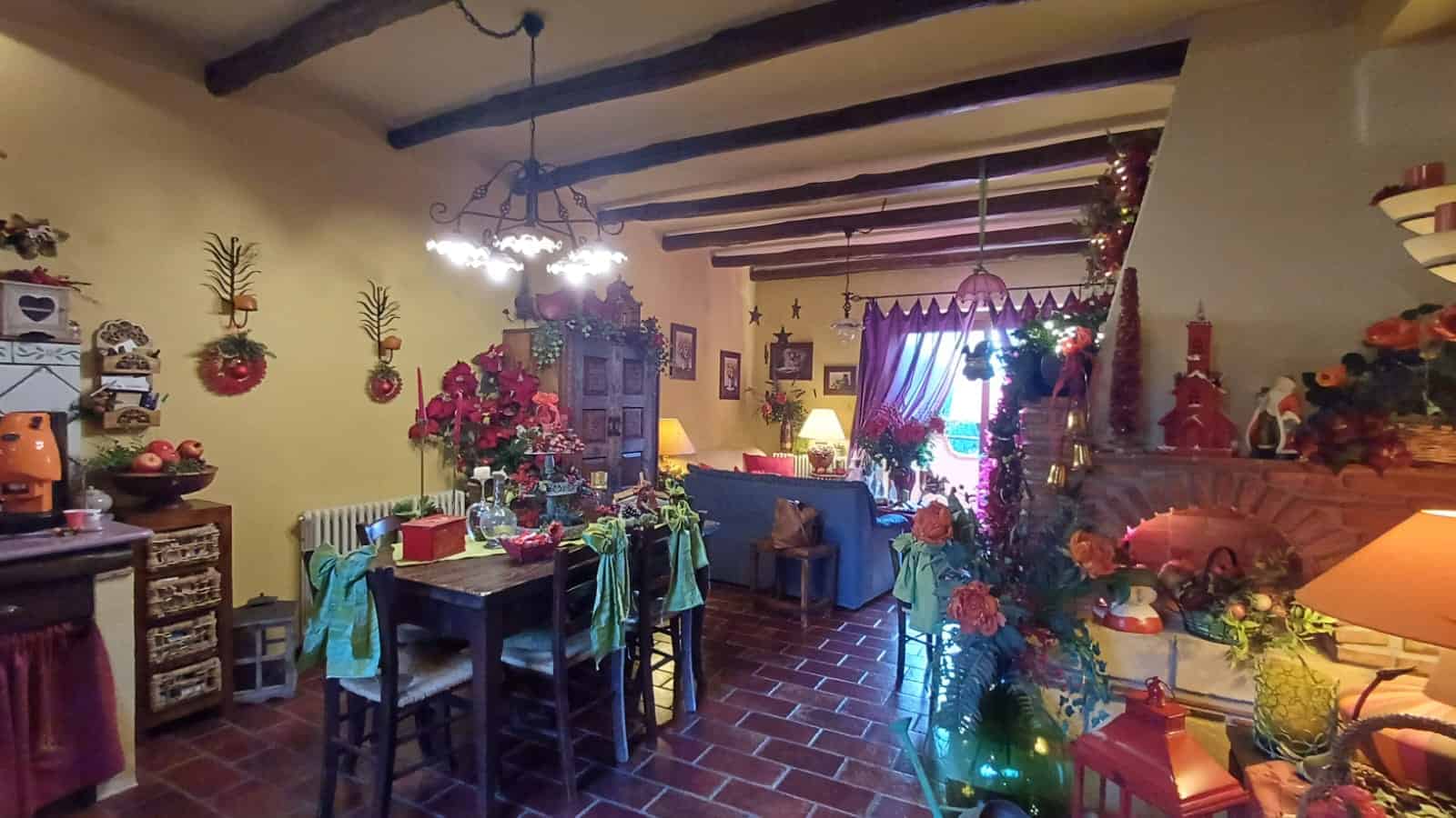 1. Interno soggiorno natalizio decorato con luci, addobbi e festoni, atmosfera calda e accogliente con travi in legno e arredi tradizionali, perfetto per le feste.