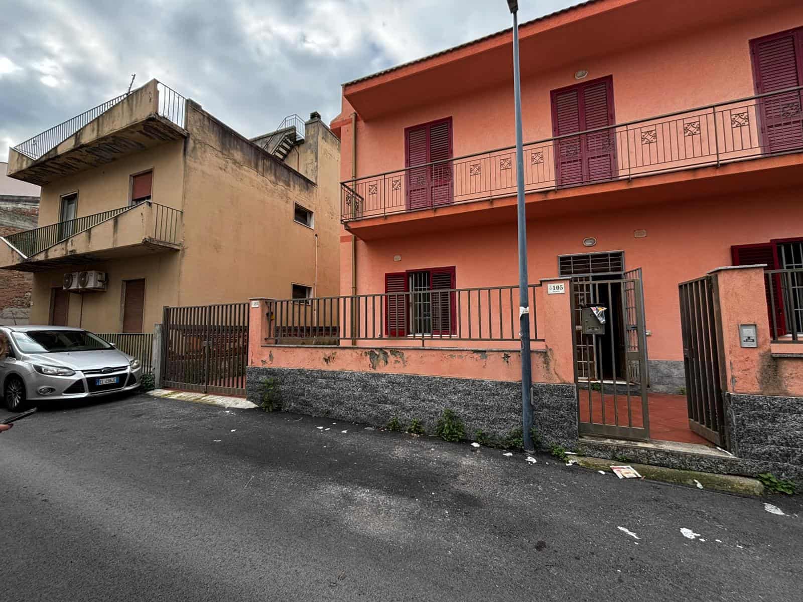Casa in affitto con cortile e balconi, edificio in stile mediterraneo con facciata rosa, serramenti rossi, area parcheggio, ambiente urbano vicino a servizi. Ideale per famiglie e professionisti in centro città.