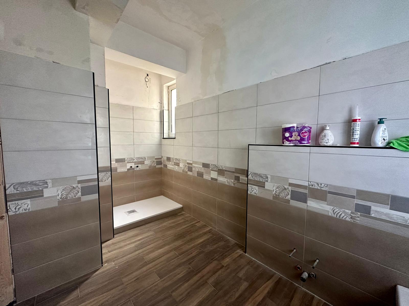 Box doccia in costruzione con pareti piastrellate, finestra naturale, dettagli di rivestimento moderno, ambiente bagno in fase di completamento, soluzione per ristrutturazione di casa.