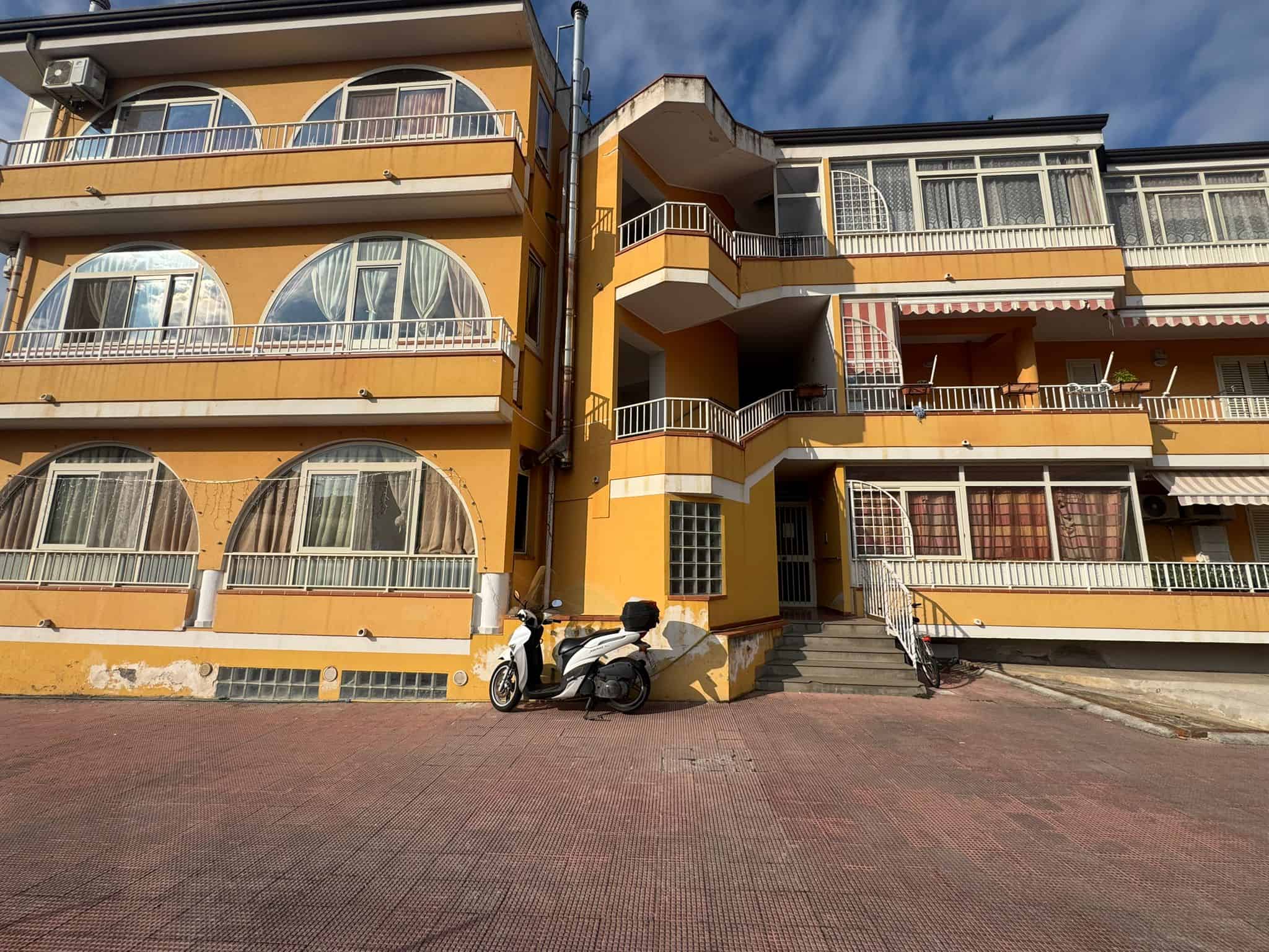 Appartamento in vendita in edificio con balconi e grandi vetrate, zona centrale, con scooter parcheggiato davanti e scale d'accesso, ideale per investimenti immobiliari in Italia.