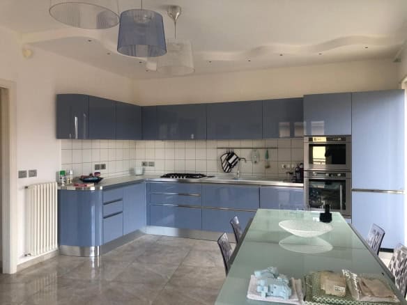 1. Cucina moderna con ante azzurre lucide, piano in acciaio inox e soggiorno luminoso, ideale per case di lusso o appartamenti eleganti.
