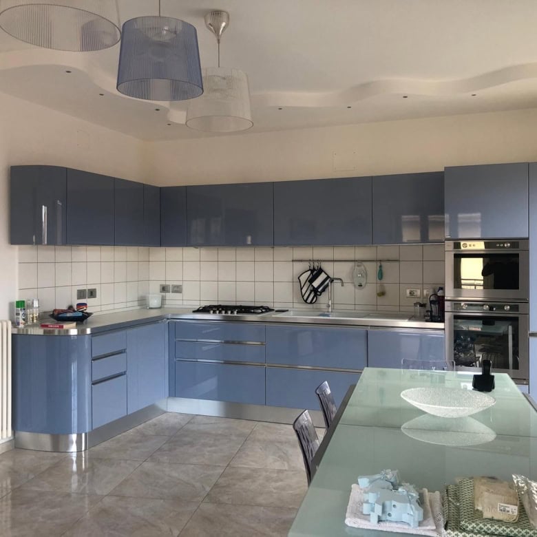 1. Cucina moderna con ante azzurre lucide, piano in acciaio inox e soggiorno luminoso, ideale per case di lusso o appartamenti eleganti.