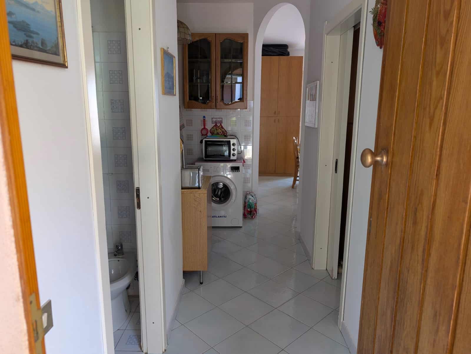 Lavanderia e cucina compatta in appartamento NextCasa con elettrodomestici funzionali e arredi in legno.