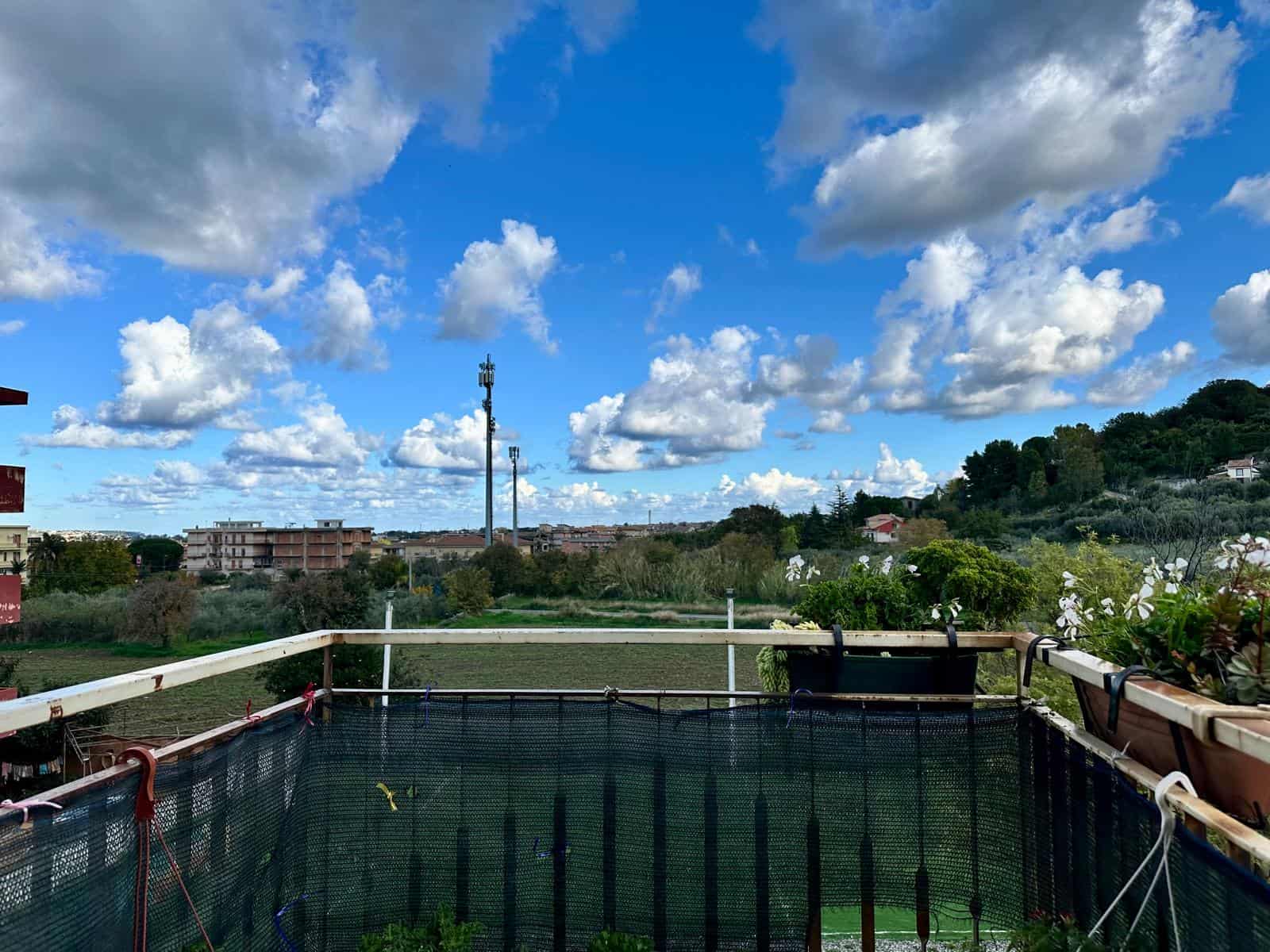 Paesaggio urbano con cielo nuvoloso, vista panoramica da balcone con piante e fiori, riflesso naturale e ambiente tranquillo, ideale per immobili residenziali NextCasa, servizi immobiliari italiani.