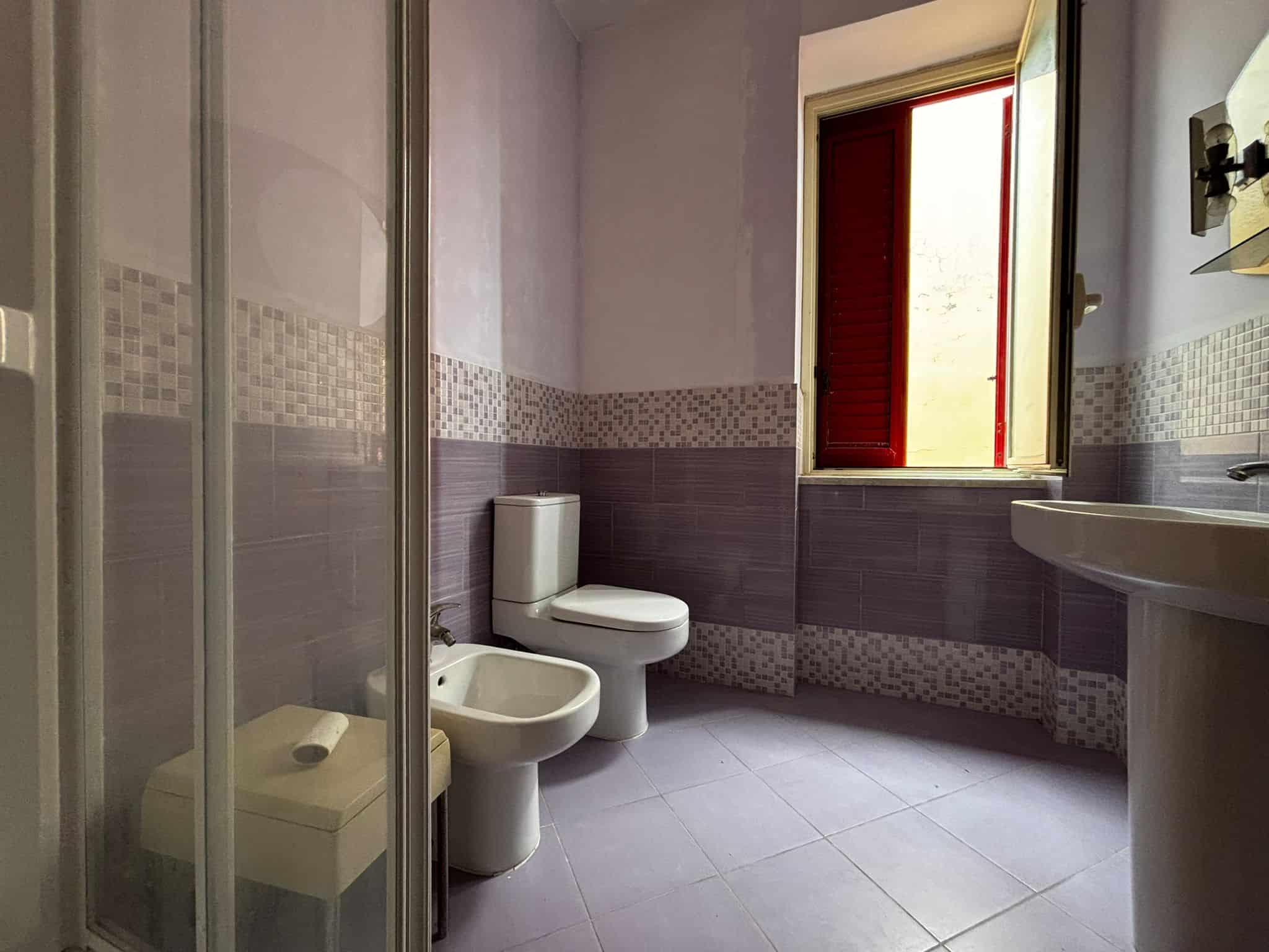 Bagno spazioso con finestra, pavimento in piastrelle lavanda, mobili moderni, perfetto per case in vendita o affitto, ambiente luminoso, dettagli eleganti, ideale per comfort e funzionalità.