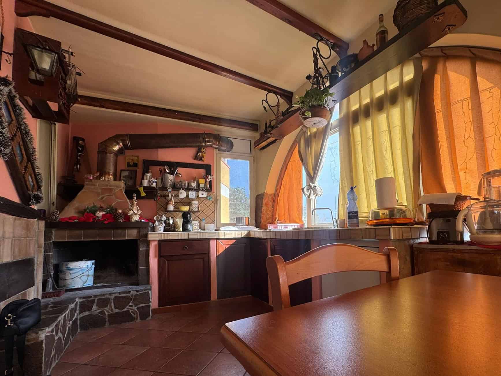 1. Cucina rustica con camino in pietra, finestre luminose con tende gialle e arancioni, decorazioni natalizie e mobili in legno, atmosfera calda e accogliente, soluzione immobiliare NextCasa.