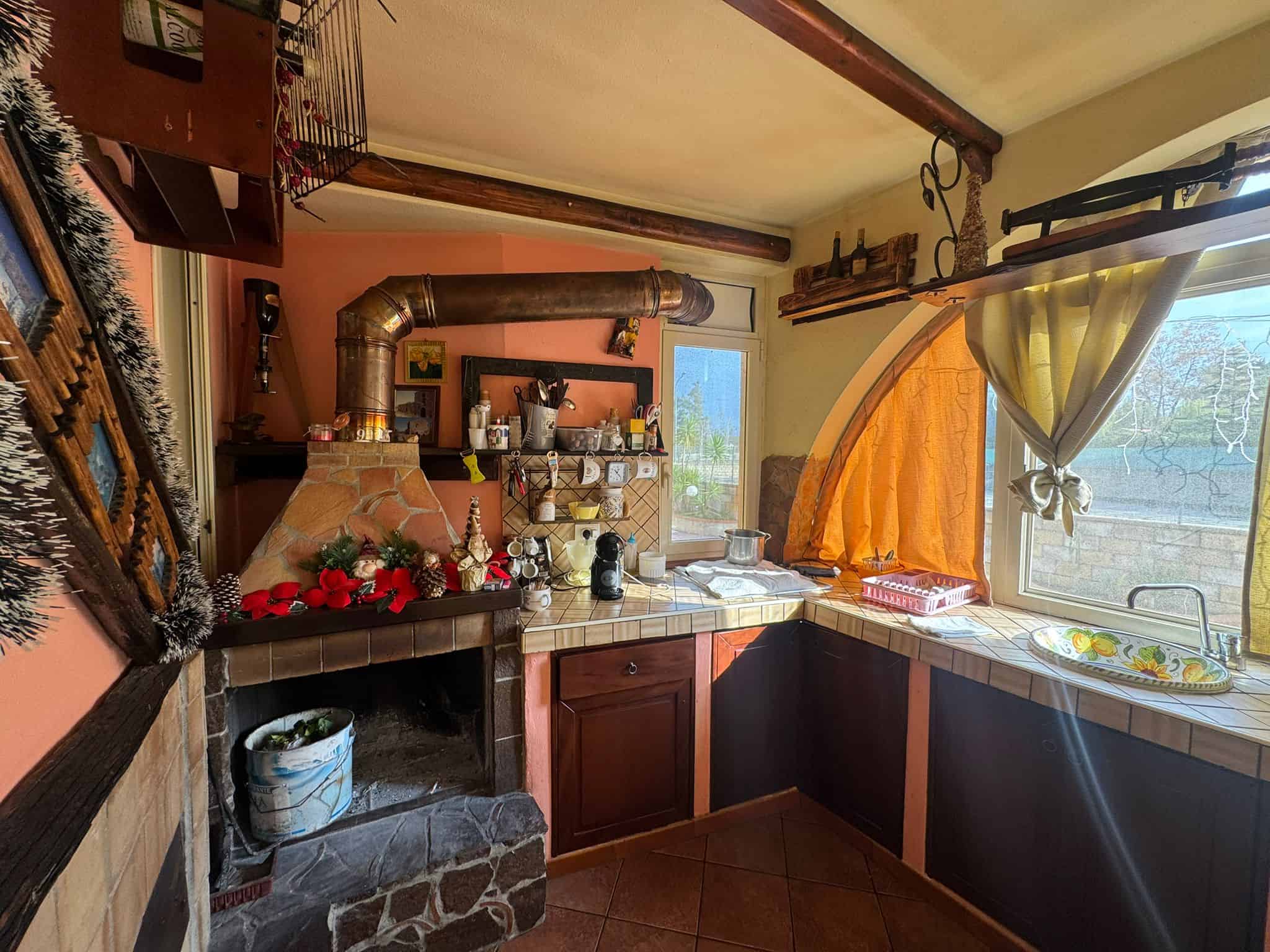 Accogliente cucina rustica con camino, dettagli in legno, pareti colorate e tende di tessuto creando un'atmosfera calda e invitante. Perfetta per momenti conviviali e cucina casalinga.