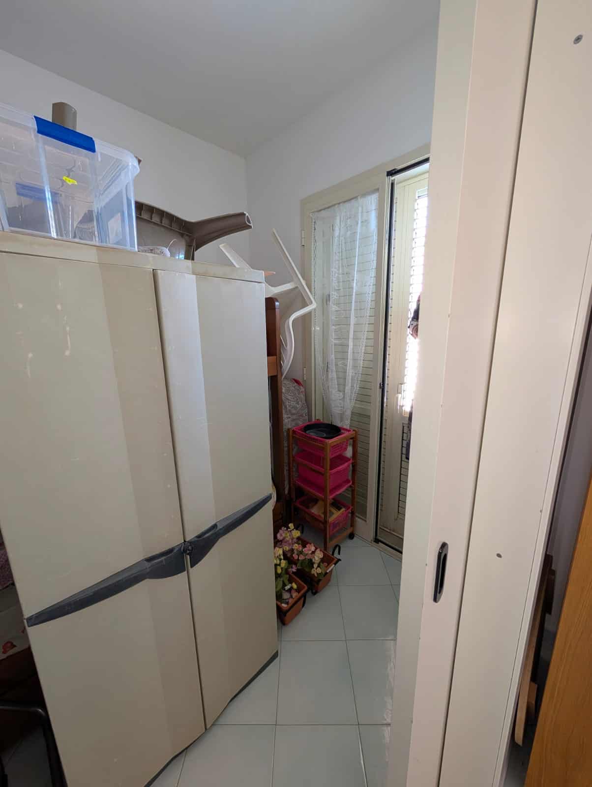 Pannello di lavanderia con armadio, scaffale rosa e piante in vaso vicino a porta finestra, arredo pratico e funzionale per ottimizzare gli spazi in casa.