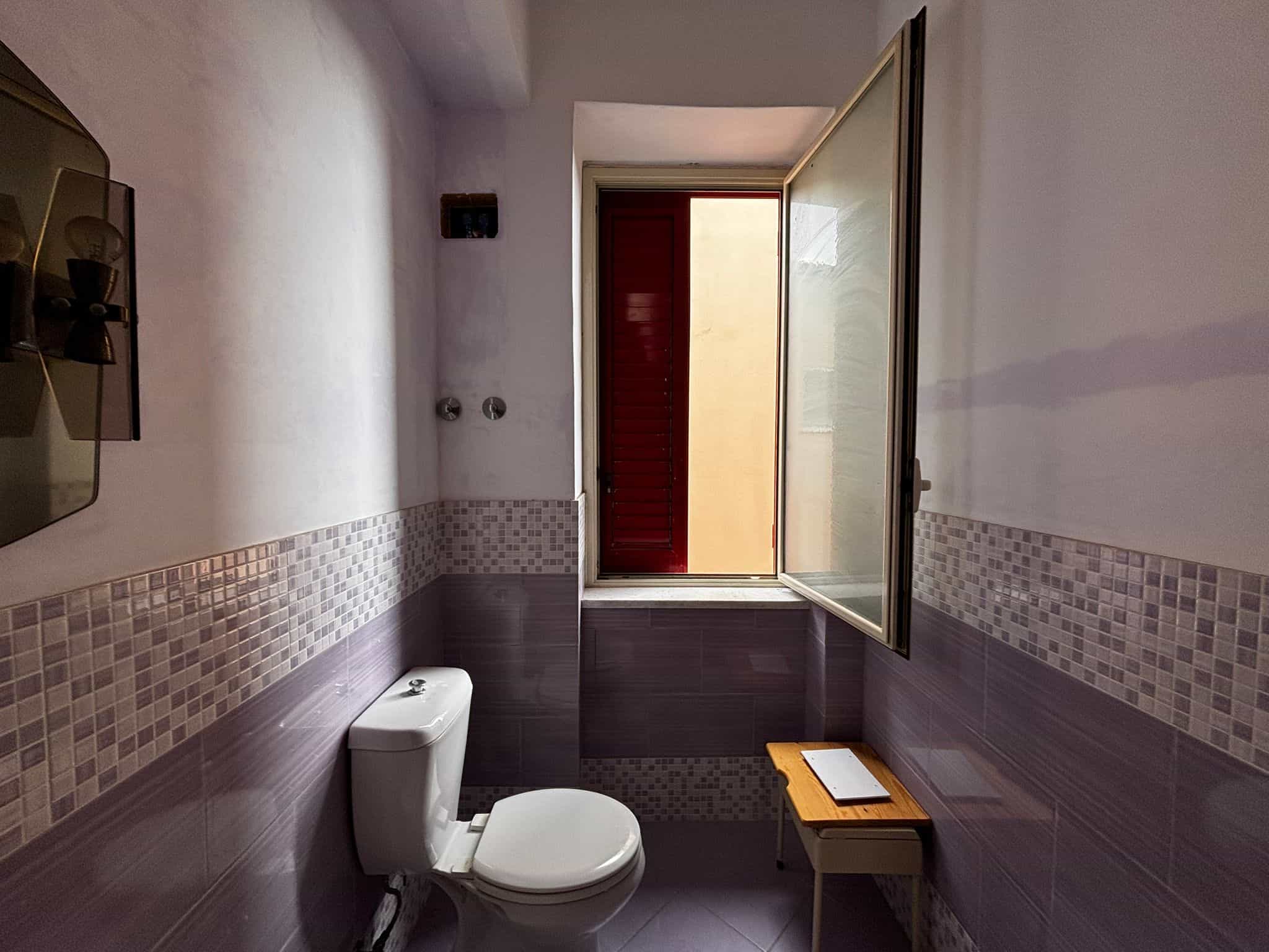 Vista bagno con finestra, sanitari moderni, piastrelle beige e viola, spazio luminoso, ideale per appartamenti in vendita o affitto, stile semplice e funzionale, atmosfera accogliente.