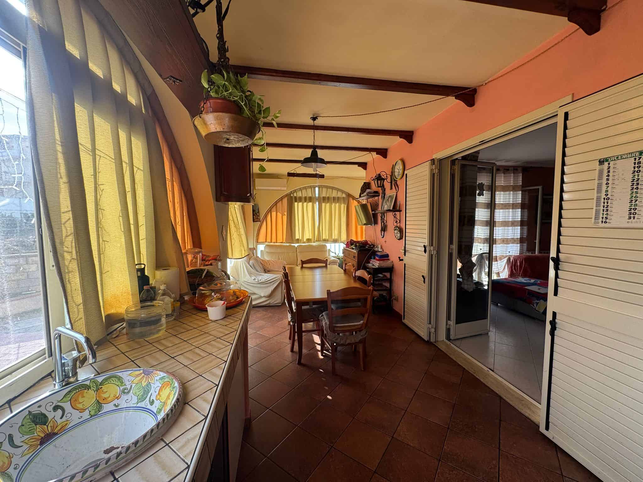 Balcone o veranda con grandi finestroni, decorato con tende di lino gialle e arancio, con mobili in stile rustico e dettagli vintage, ideale per vivere lo spazio esterno in casa.