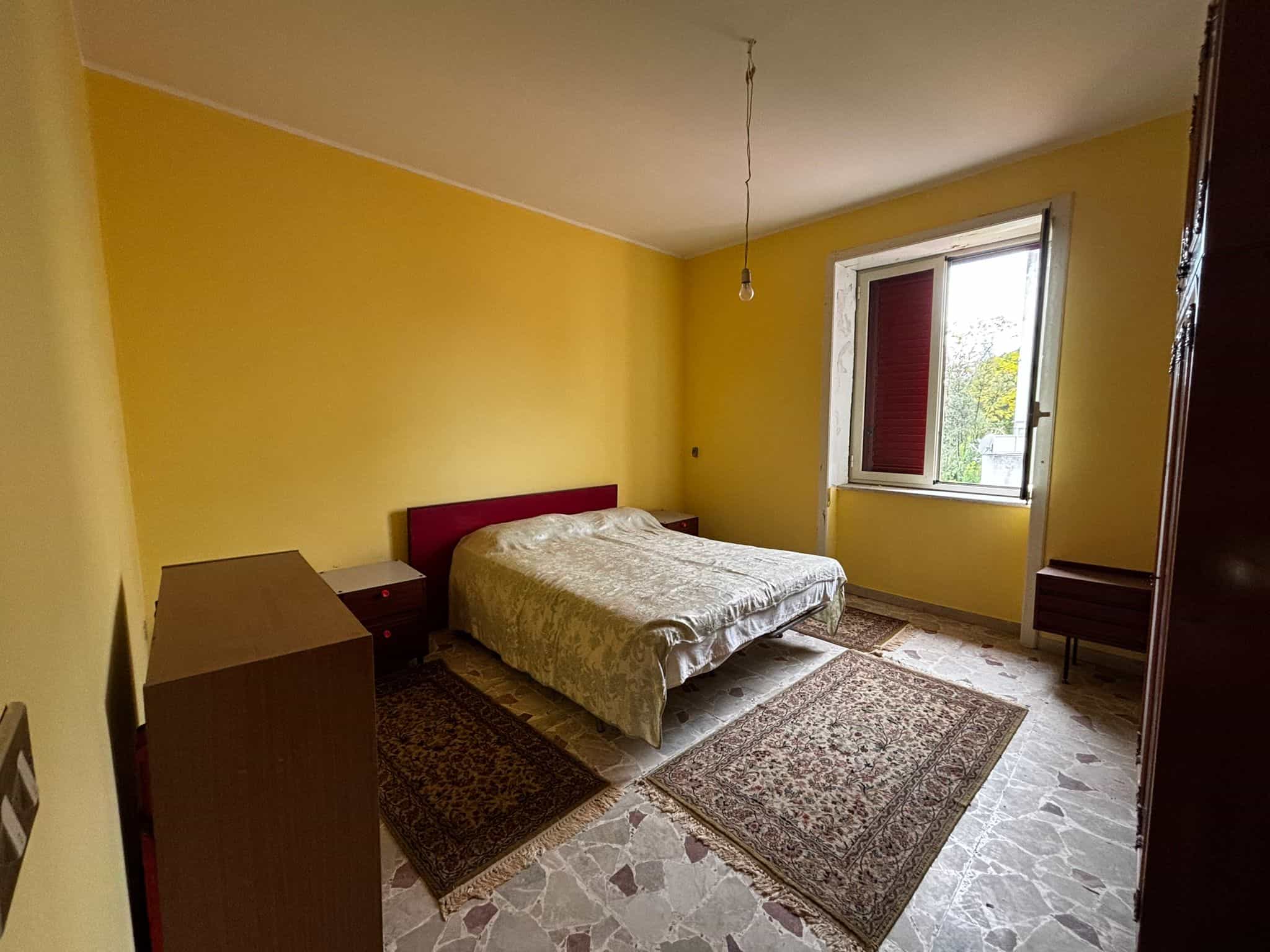 Ampio soggiorno con pareti gialle, letto matrimoniale e mobili vintage, illuminato da luce naturale dalla finestra lato est, ideale per vivere in comfort e stile, perfetto per chi cerca una casa accogliente e luminosa.