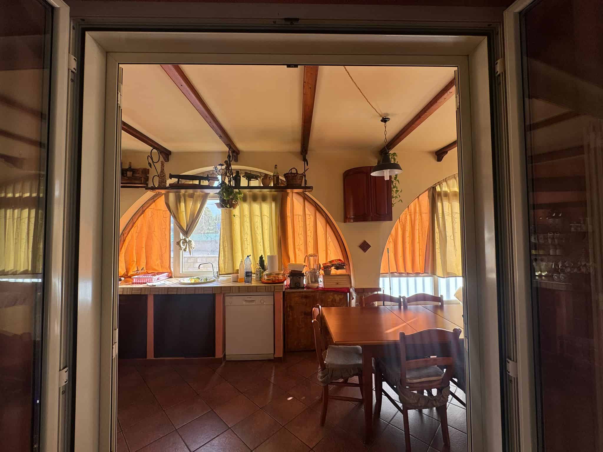 Ampia cucina open space con finestre ad arco, tende colorate e mobili in legno, ideata per ambienti accoglienti e funzionali, perfetta per vivere momenti conviviali.