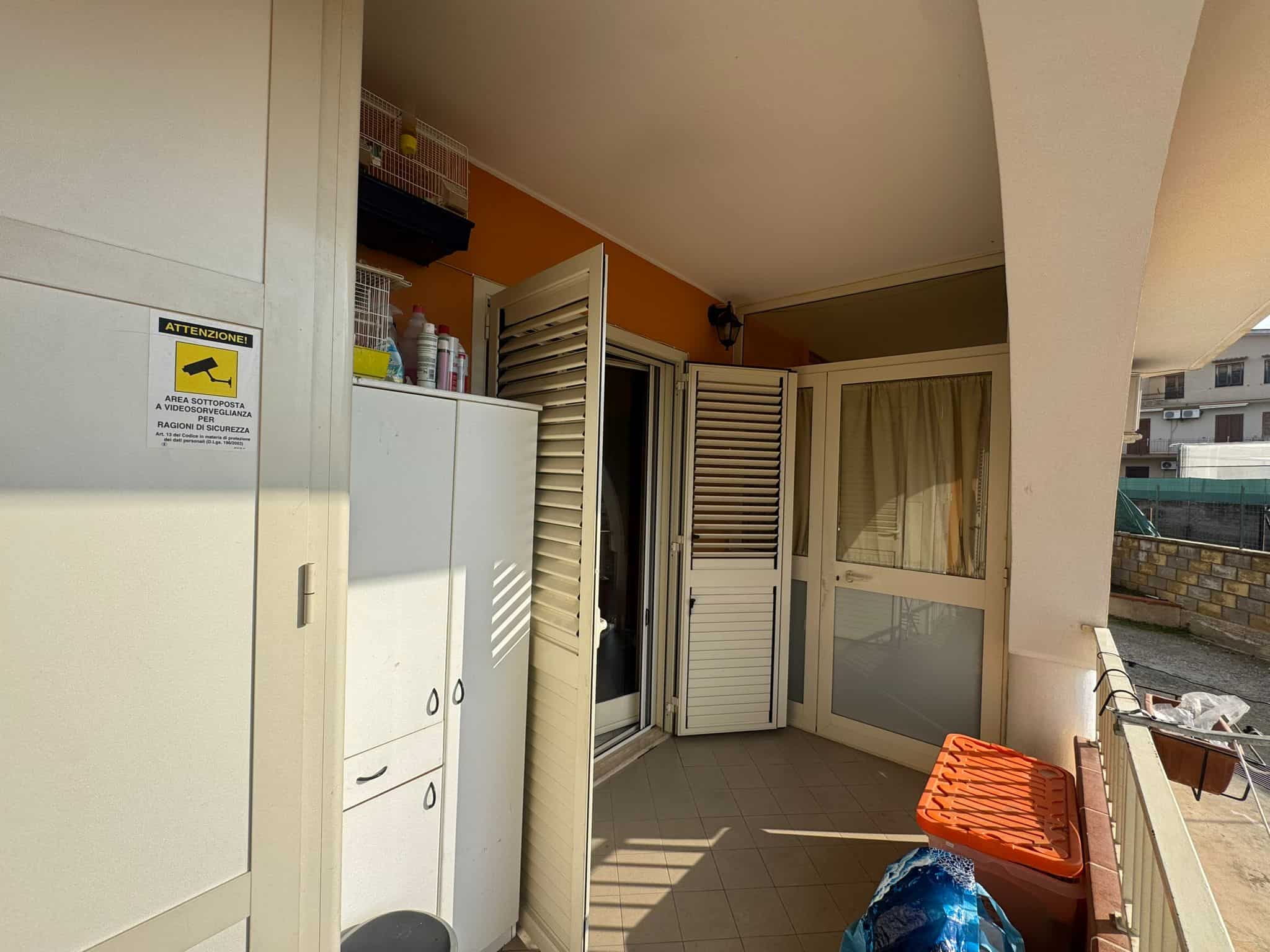 Balcone di appartamento con arredi, serramenti scorrevoli e vista su cortile interno, ideale per relax e lavanderia, con spazio per stendere e conservare oggetti, in zona residenziale.