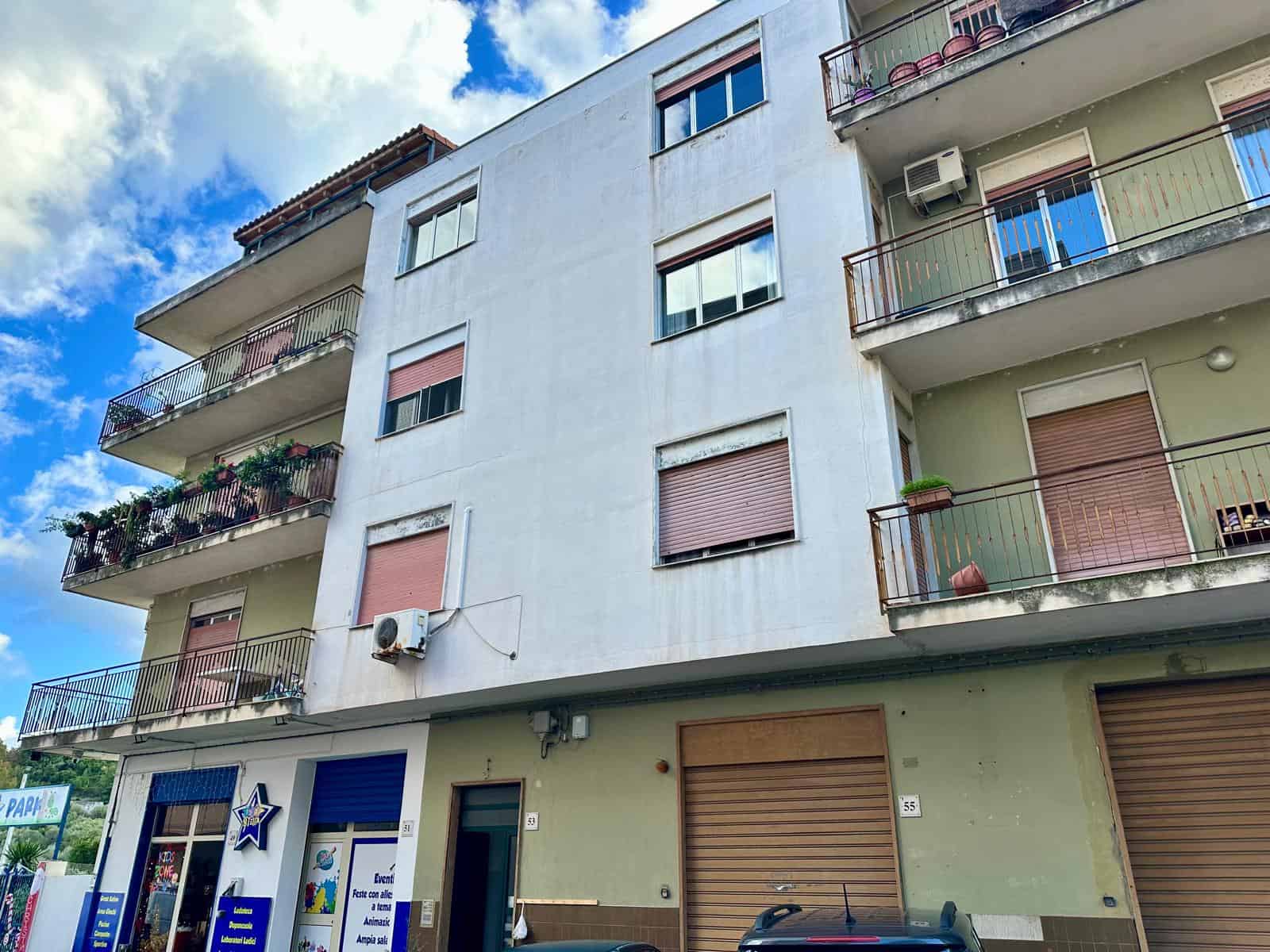 Appartamenti con balconi moderni in edificio residenziale a due piani, con negozio al pian terreno, in zona urbana con parcheggio e atmosfera vivace.