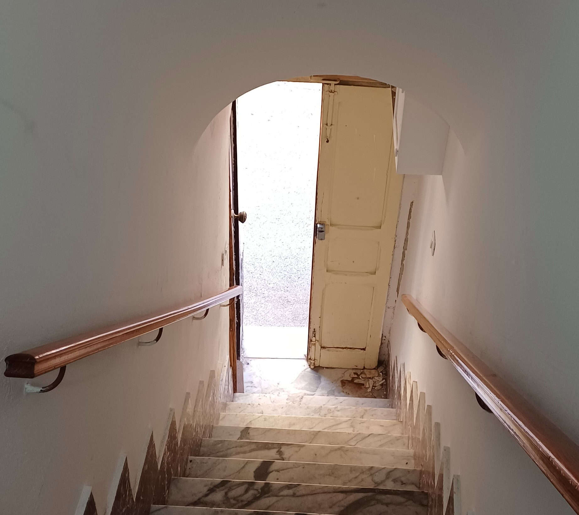 Scala interna in marmo con ringhiera in legno, ingresso di una proprietà immobiliare, passaggio tra diversi piani in contesto residenziale.