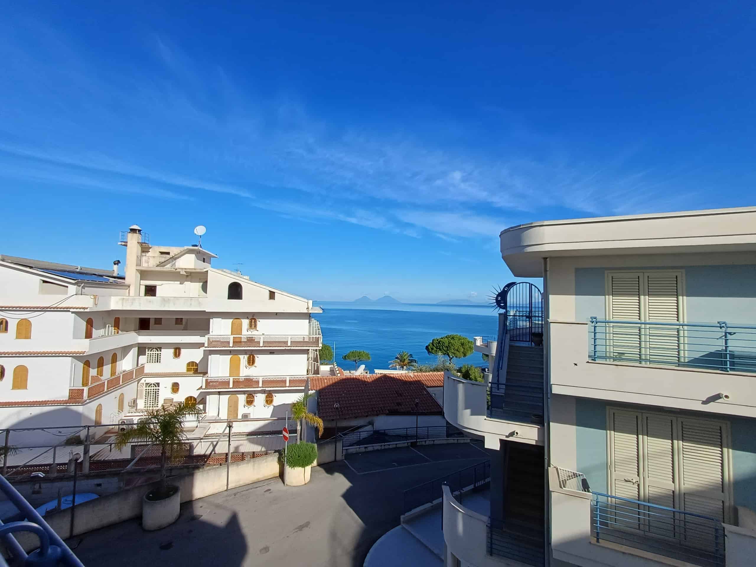 Vista mare dal balcone con condomini e cielo azzurro, ispirazione per immobili di lusso e appartamenti sul mare a Napoli, ideale per promuovere immobili residenziali fronte mare e viste panoramiche.