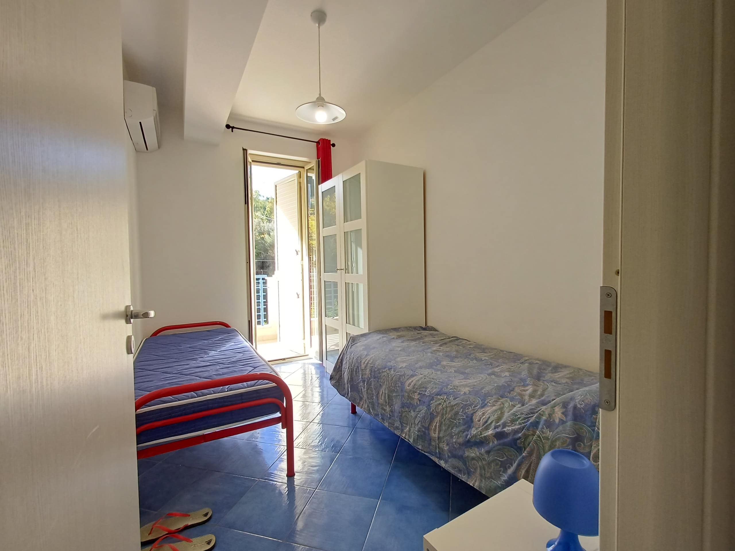 Camere da letto in affitto con vista su balcone, arredate con letto singolo e spazio per relax, in ambiente luminoso con aria condizionata e decorazioni semplici.