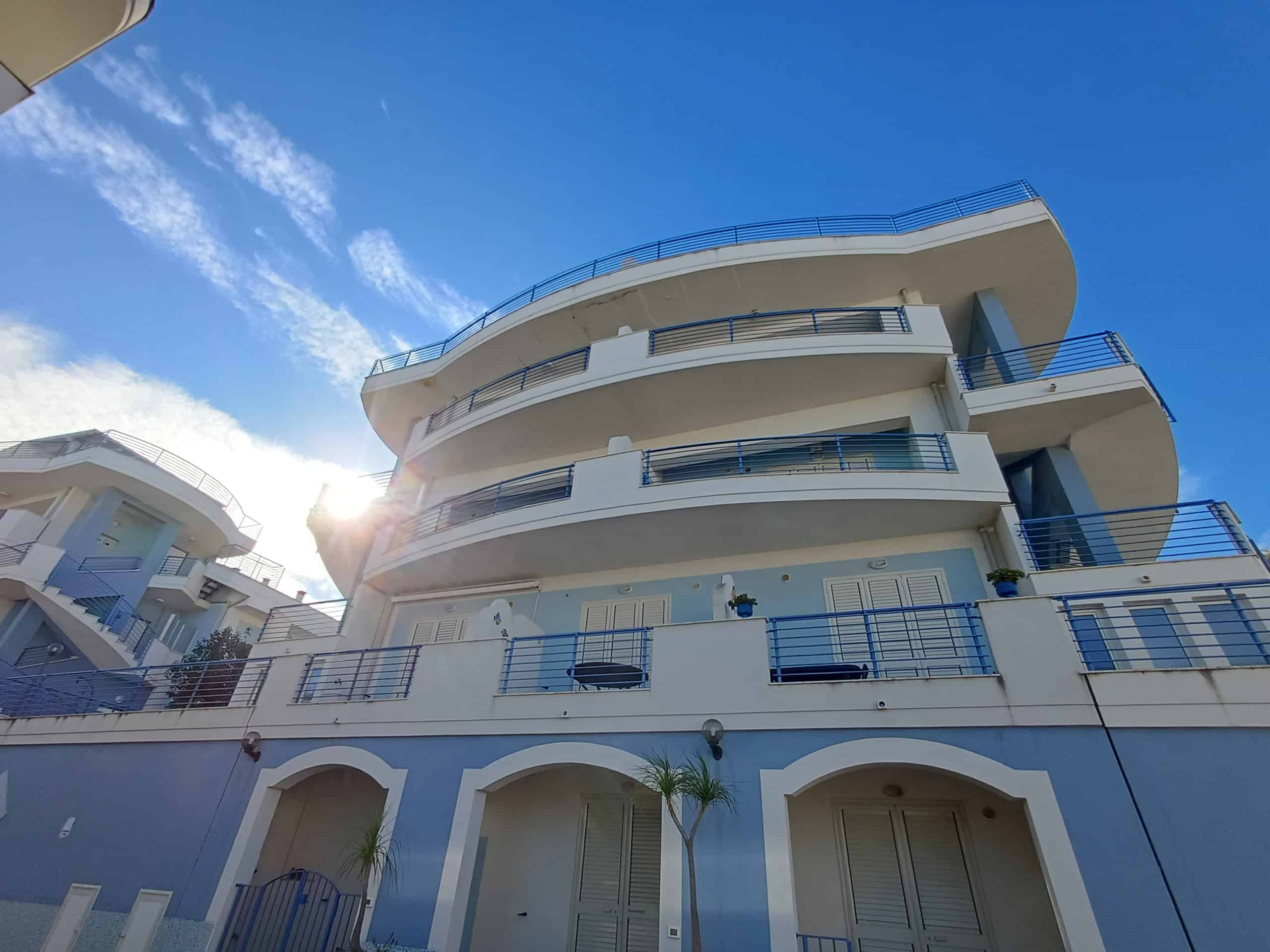 Balconi di edificio residenziale con struttura moderna e dettagli in blu, sotto un cielo limpido e soleggiato, caratteristiche tipiche di immobili di qualità, ideale per offerte immobiliari.