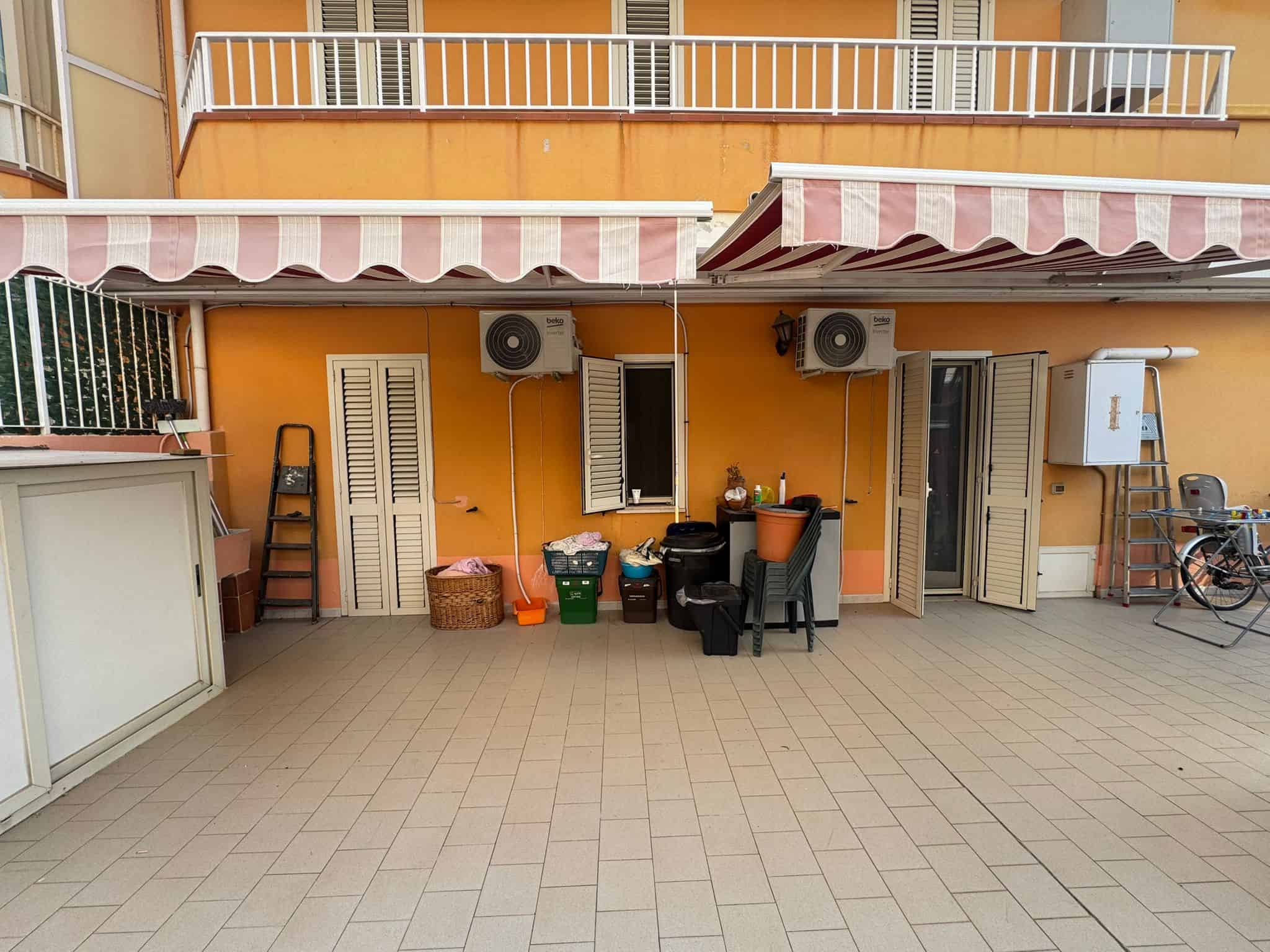 Terrazza con arredi e tende da sole, vista di balconi di un appartamento, spazio esterno con oggetti vari e aria condizionata, ambiente abitativo esterno, NextCasa, soluzione immobiliare.