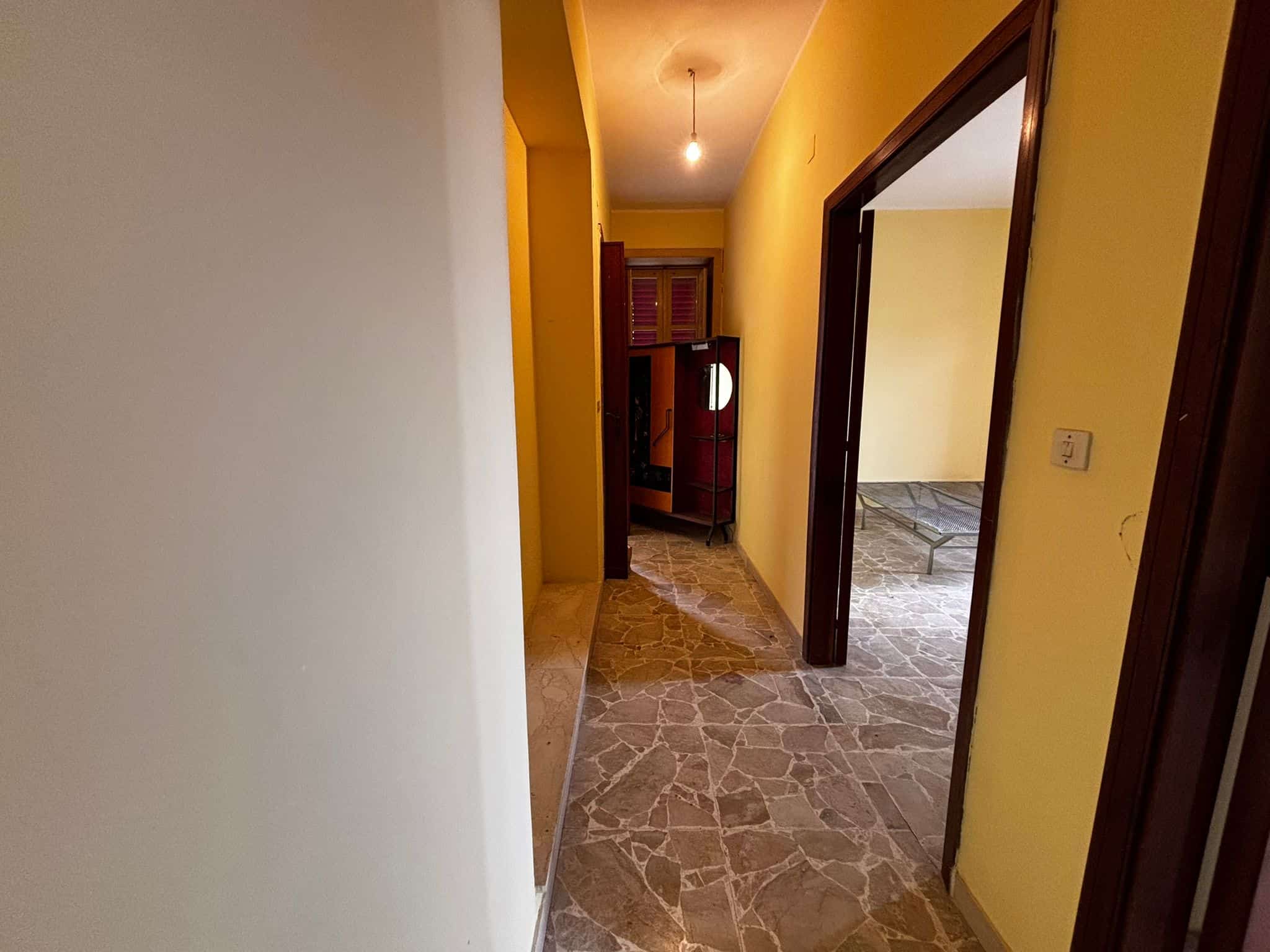 Spaziatura di un corridoio luminoso in un appartamento con pareti gialle e pavimento in piastrelle di pietra, interni tradizionali, perfetta per affitti e vendite immobiliari.