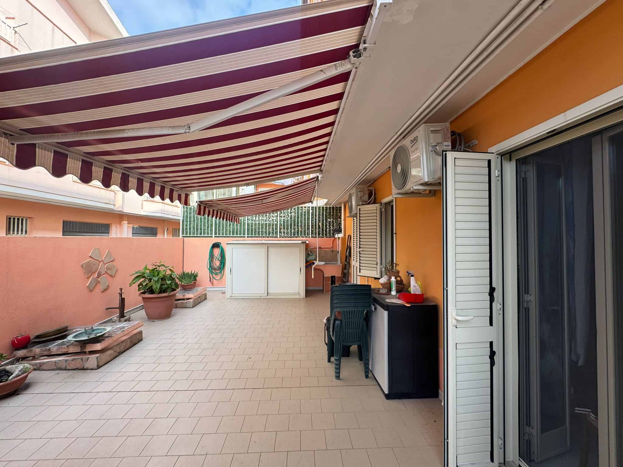 Ampio terrazzo con tenda retrattile a strisce, piante, mobili da esterno e vista sulla zona circostante, ideale per relax e convivialità, zona living esterna, immobiliare NextCasa.