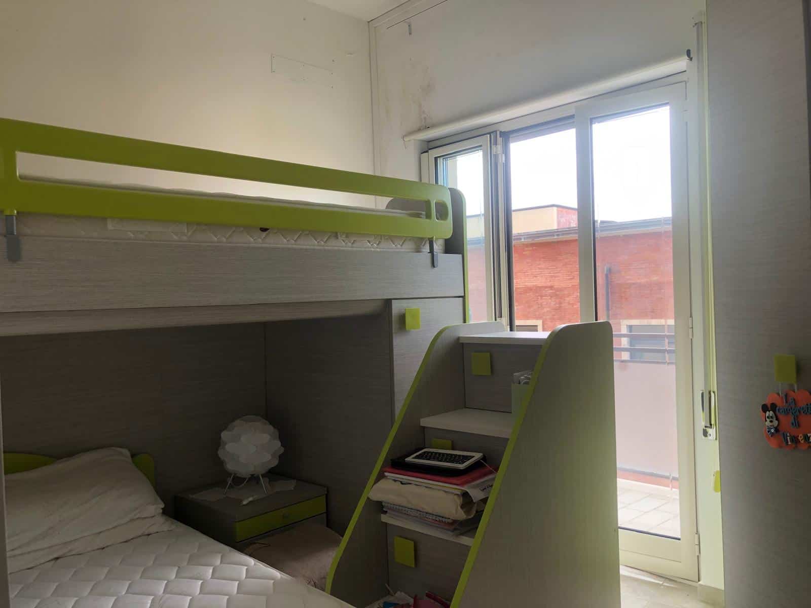 Letto a castello in camera con ampie finestre, dotato di scrivania e scaffale; ideale per soluzioni di arredamento e mobili casa NextCasa.