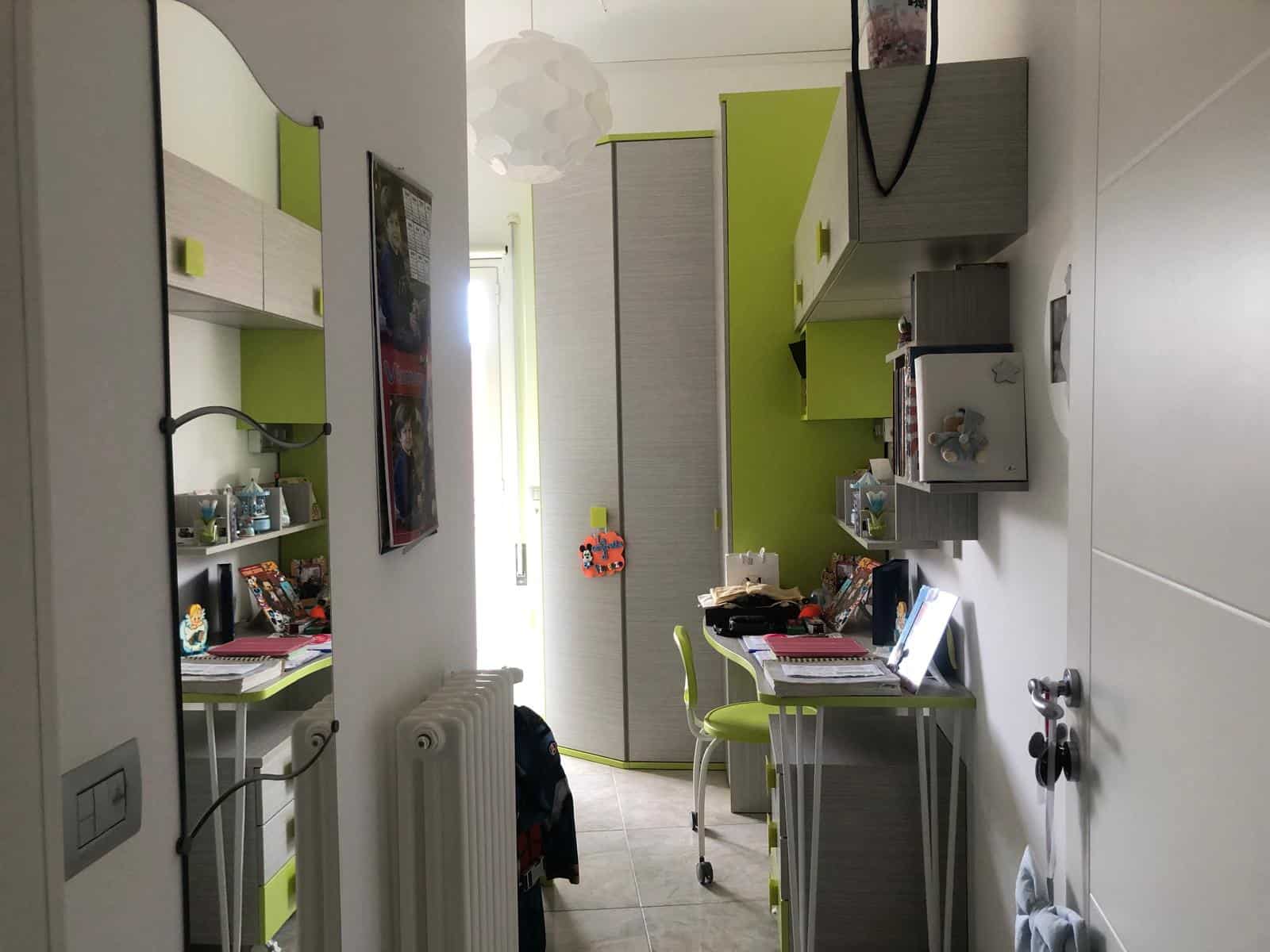 Arredamento per cameretta bambini con mobili moderni in grigio e verde, scrivanie, armadi e decorazioni ludiche per ambienti funzionali e accoglienti.
