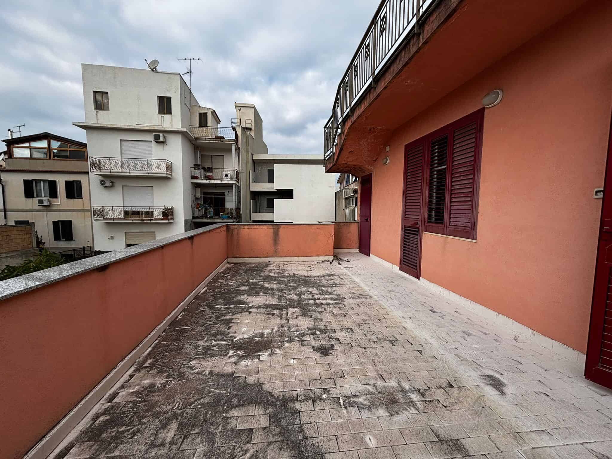 Ampio terrazzo urbano con vista su edifici residenziali, superficie in piastrelle e parapetto in muratura, ideale per relax e momenti di socializzazione, in un quartiere vivace e ben collegato.