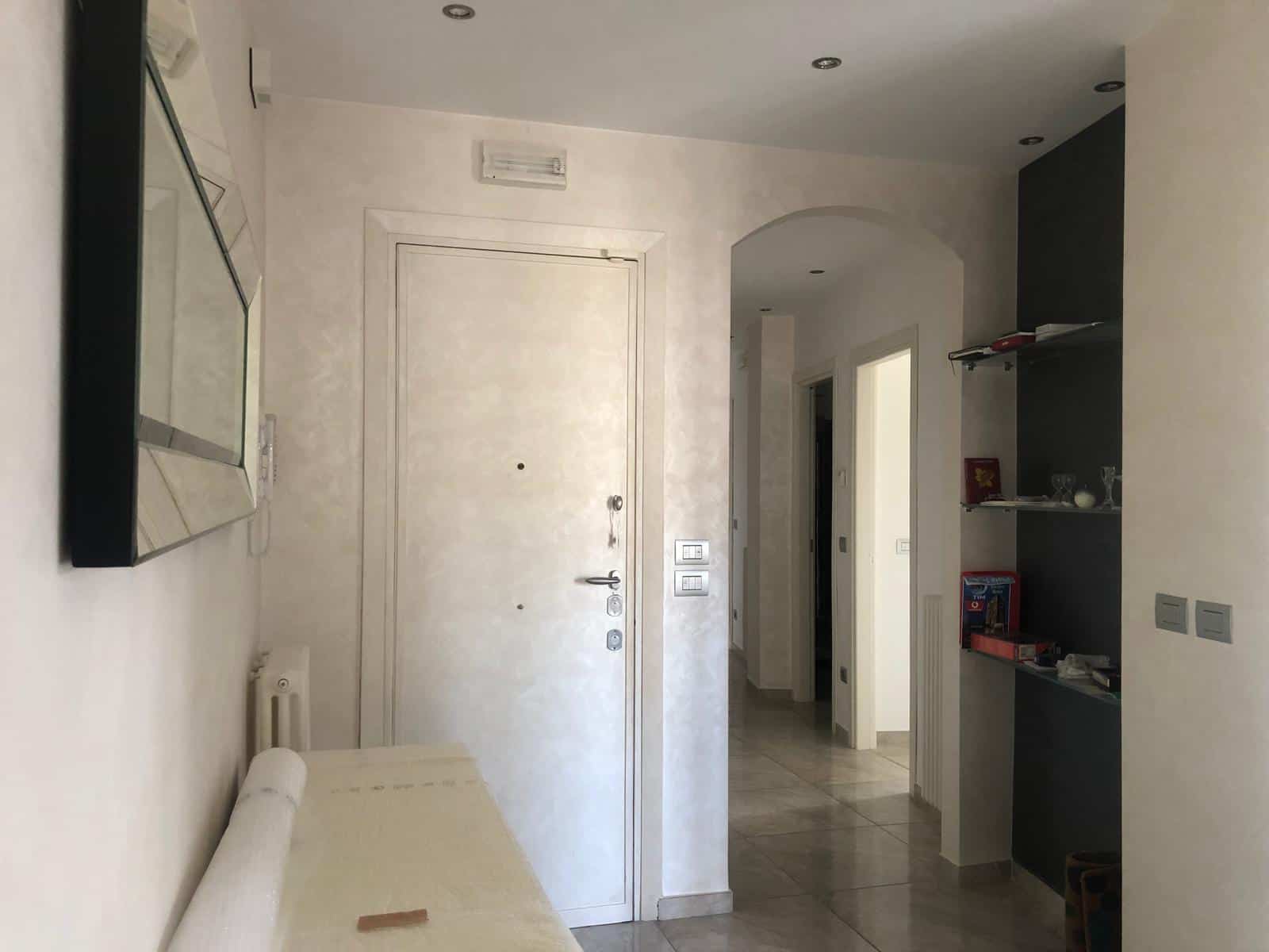 Porta d'ingresso di un appartamento moderno, interni luminosi con pareti chiare, dettagli di arredo minimalista e spazio ben organizzato, ideale per affitti e vendite immobiliari di qualità.