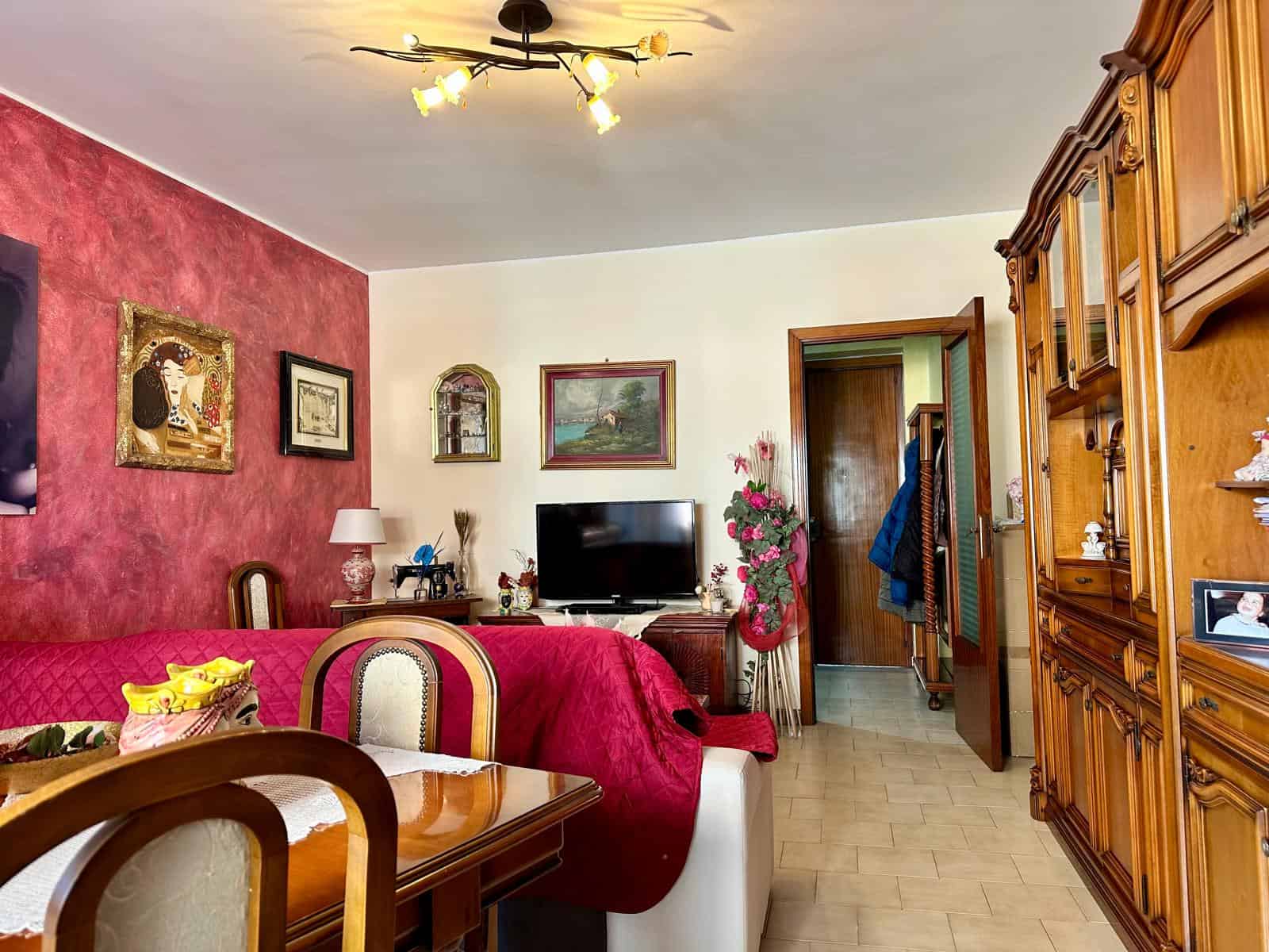 1. Interno soggiorno accogliente con arredi classici, parete rossa decorata, TV e oggetti d'antiquariato, atmosfera calda e familiare di una casa ben arredata.