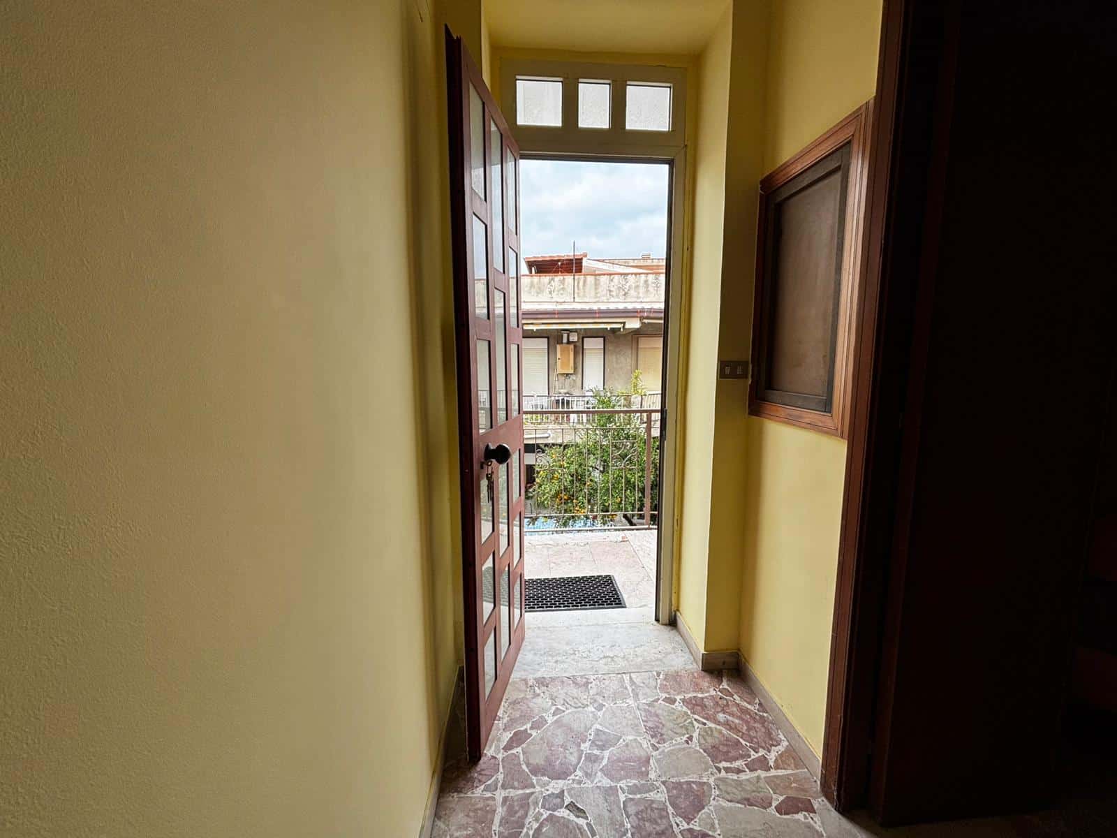 1. Porta d'ingresso in legno con finestra, vista su balcone e città, interni di casa luminosa, stile classico, ingresso con pavimento in marmo colorato, ambiente accogliente e funzionale.