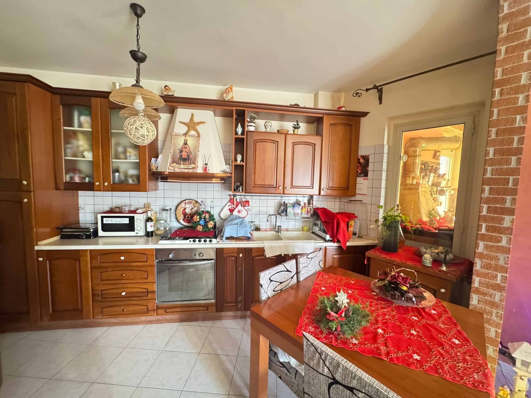 Può essere usato come esempio di una cucina abitabile con decorazioni natalizie, armadi in legno massello e dettagli festivi che migliorano l'atmosfera accogliente.