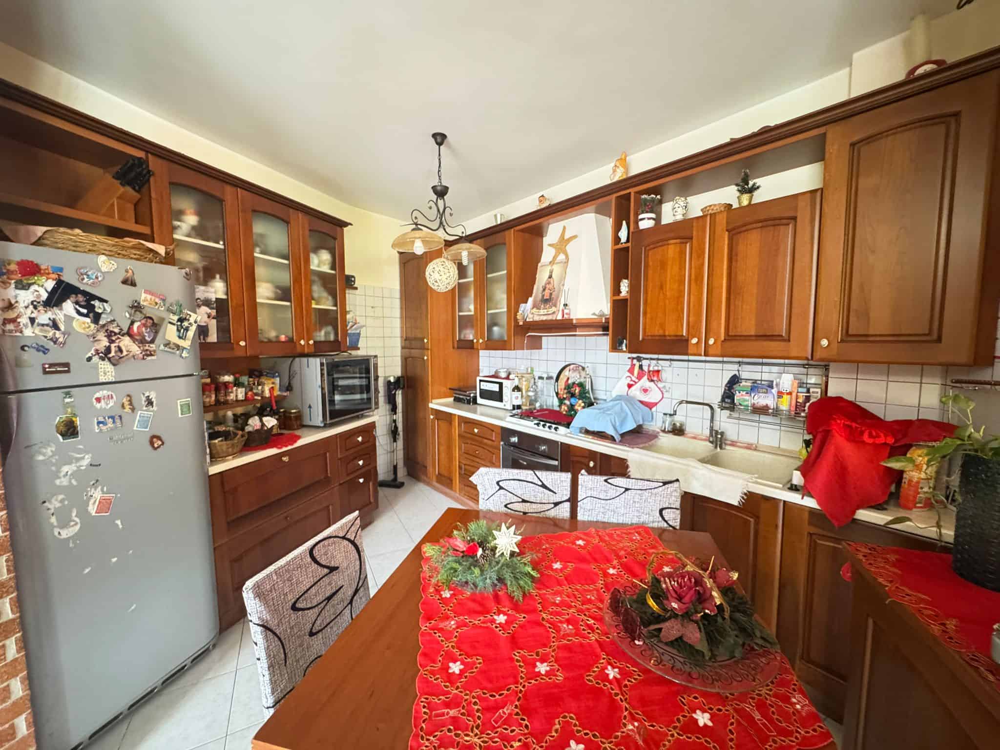 Lavagna cucina con armadietti in legno e decorazioni natalizie, frigorifero e piano cottura, ambiente accogliente e ben organizzato per la casa o l'affitto.
