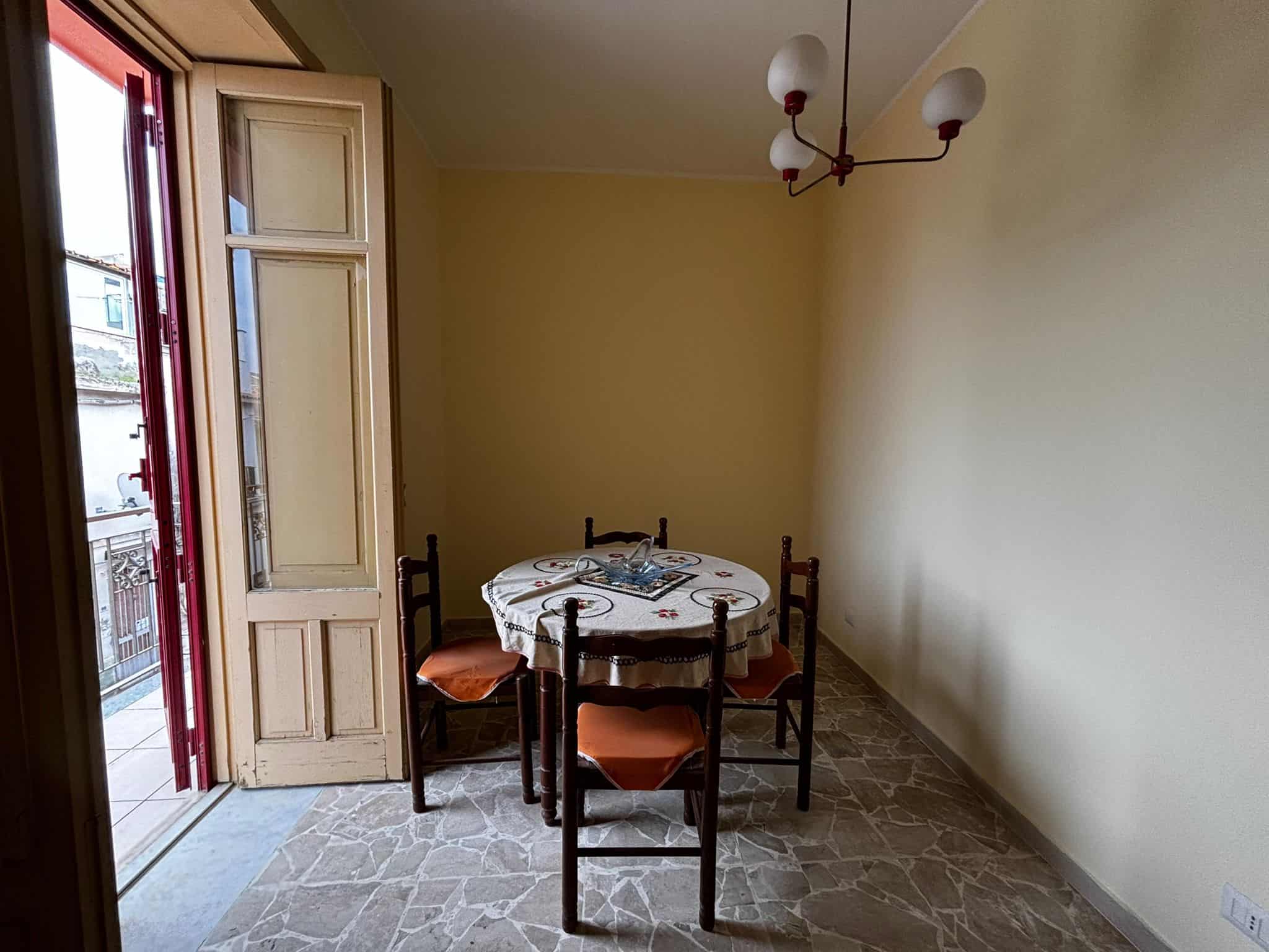 1. Tavolo da pranzo con sedie in legno nel soggiorno con balcone a Milano, stile classico, illuminato da luce naturale, arredamento semplice e accogliente.