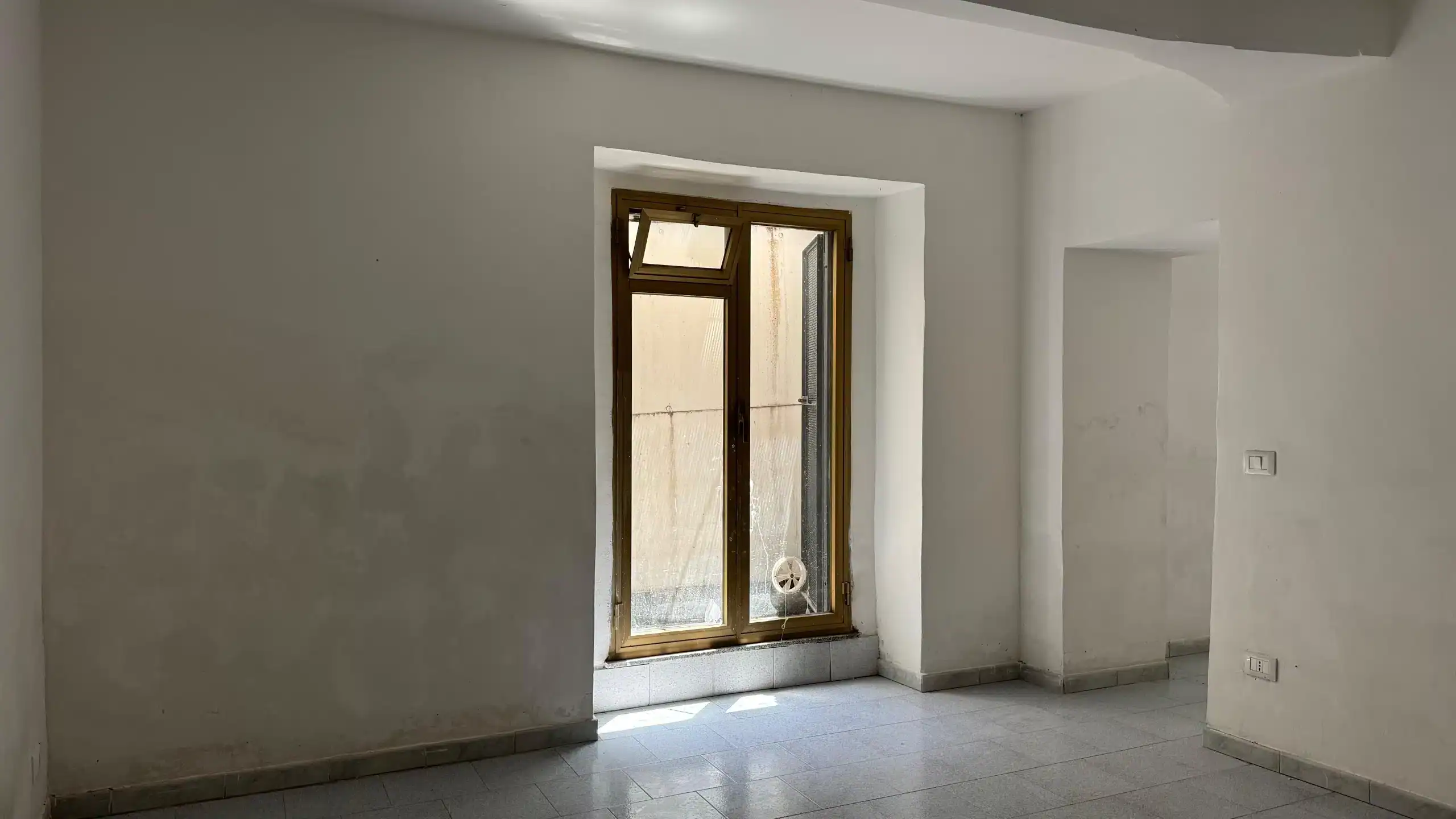 1. Finestra di una stanza in fase di renovazione con pareti bianche e pavimento in gresceramica, luce naturale, ambiente luminoso, ideale per proprietà immobiliari NextCasa.