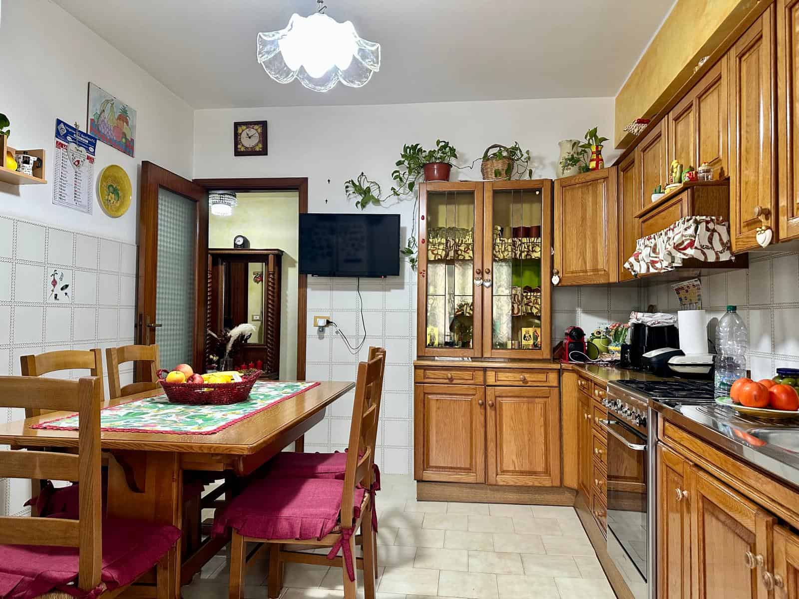 Stile classico cucina abitabile con mobili in legno, tavolo da pranzo, pareti con piastrelle bianche e decorazioni colorate, ideale per case di famiglia e servizi di affitto turistico.
