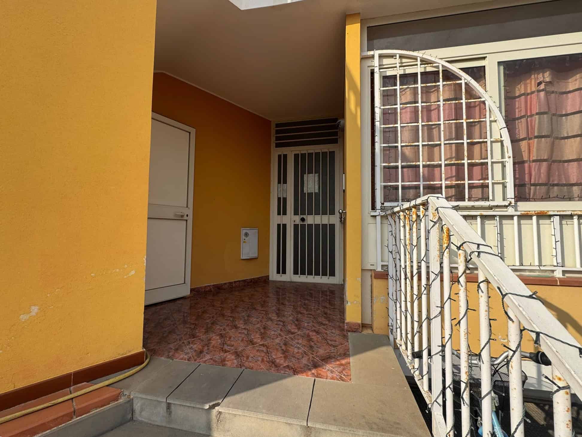 1. Varco d'ingresso di un appartamento con porta blindata, pareti gialle, pavimento in gres porcellanato con effetto marmo e ringhiera bianca decorata con luci natalizie.