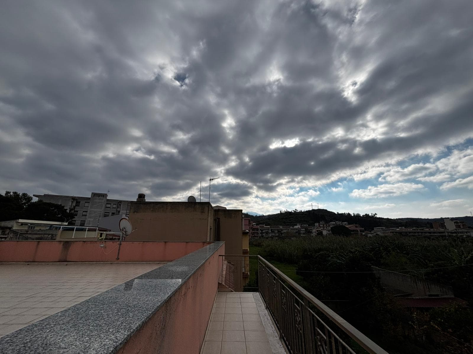 Nuvole grigie sul cielo sopra un paesaggio urbano con vista terrazza, edifici e colline in lontananza, ideale per immagini di case, immobili o viste panoramiche.