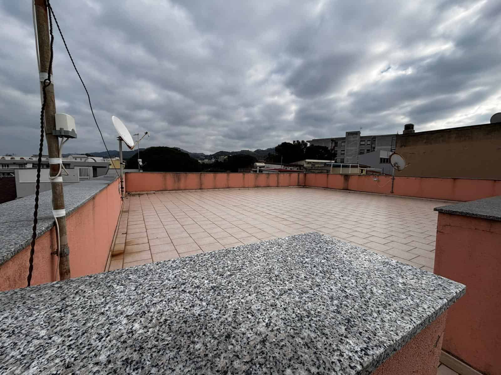 Balcone con vista panoramica su tetti e colline, spazio esterno privato ideale per relax e entertaining, coperto da nuvoloso cielo grigio, superfici in ceramica e murature in pietra.