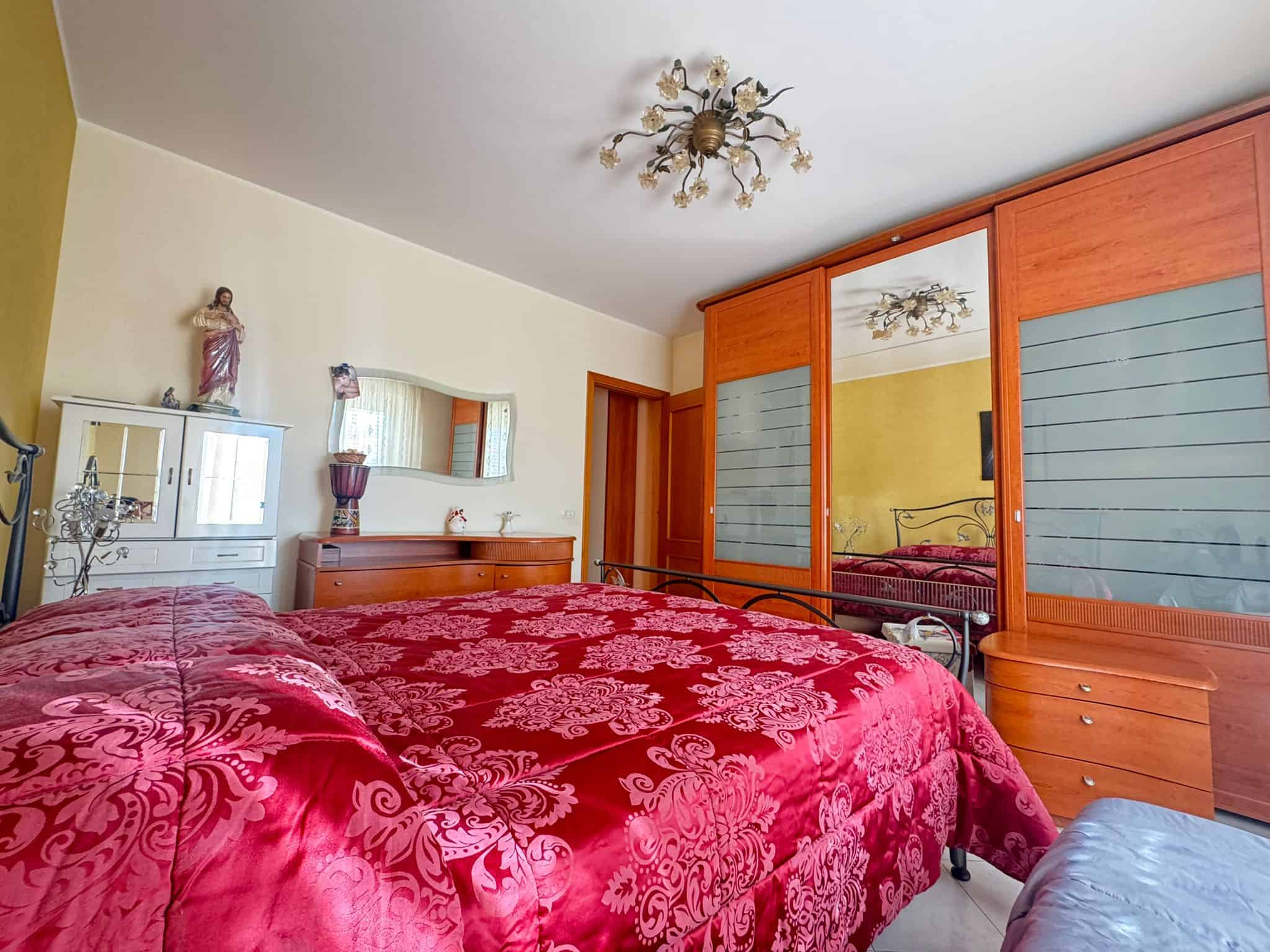 Divano letto in camera da letto matrimoniale con armadio a muro in legno e decorazioni classiche, ambiente luminoso e accogliente, ideale per offerte immobiliari e case in vendita.
