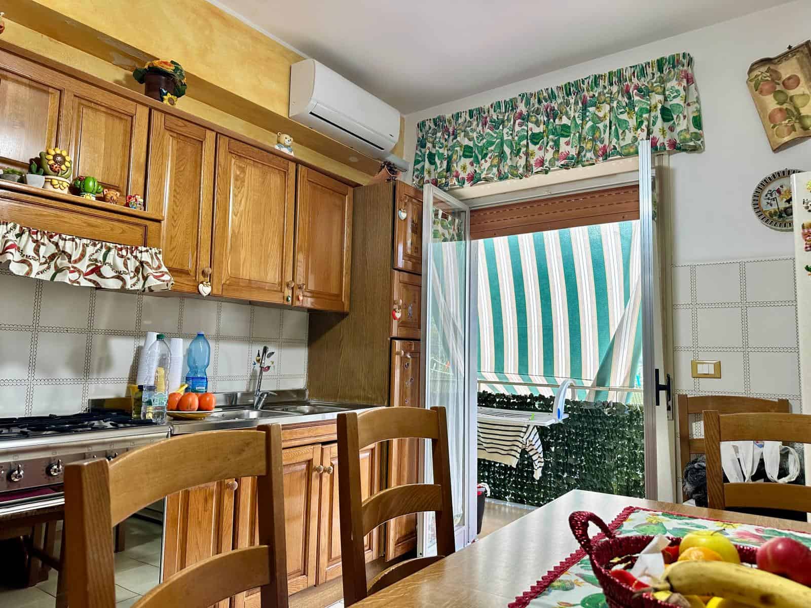 1. Cucina abitabile con mobili in legno, balcone con tenda parasole e accessori decorativi, ideale per ambienti residenziali luminosi e accoglienti.