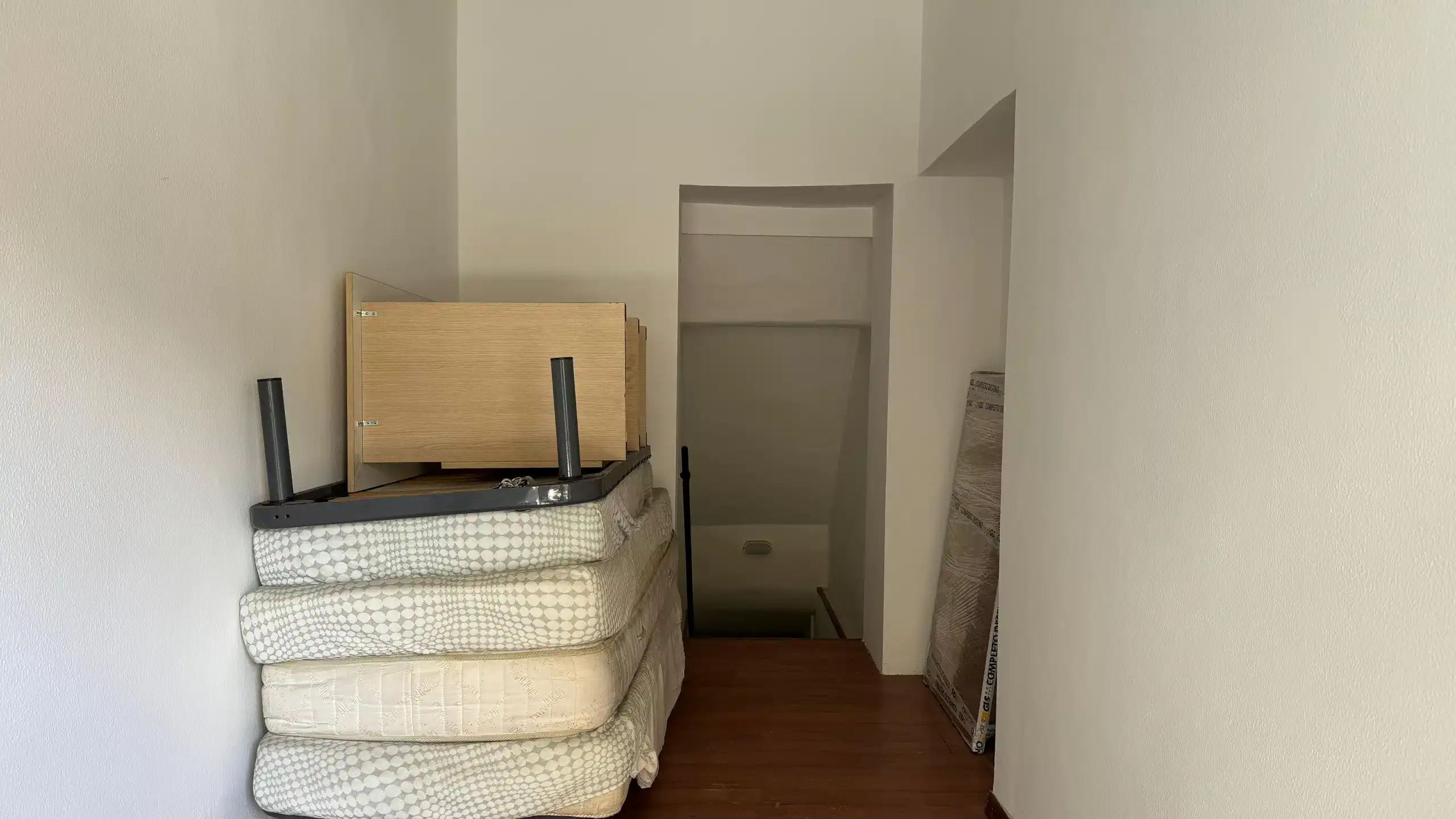 1. Maneggio di materassi e mobili di seconda mano in una stanza con pareti bianche e pavimento in legno.