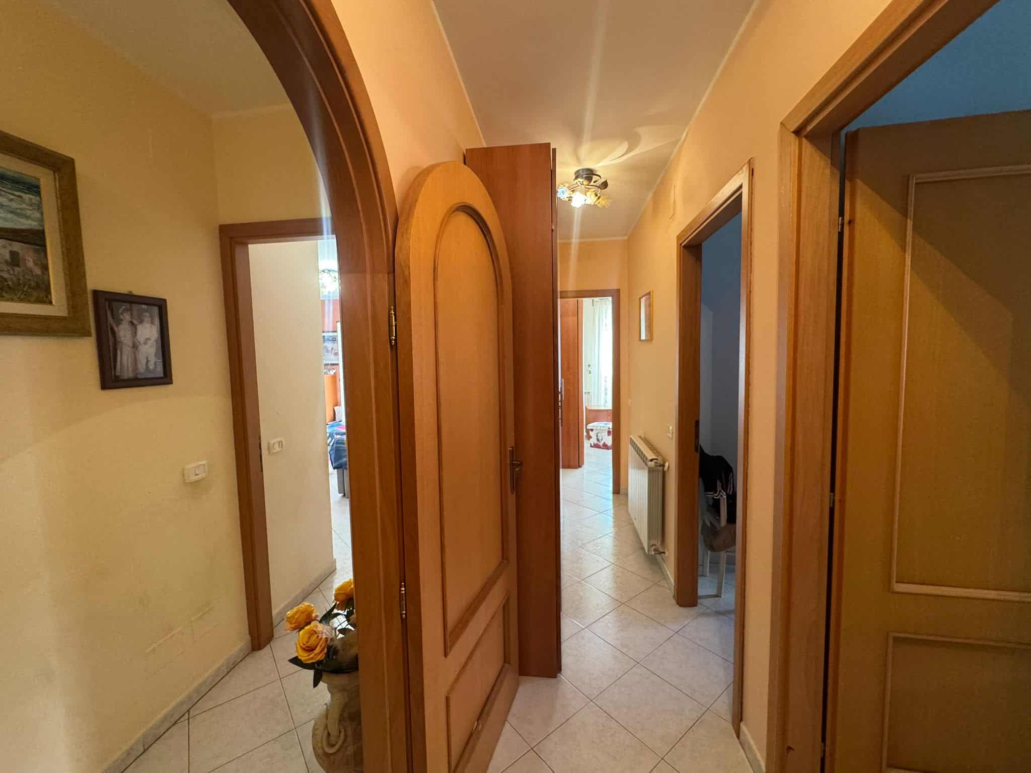 Porta di ingresso in legno con inferiore in vetro e design classico, in un corridoio con pareti gialle, quadri alle pareti e pavimento in ceramica, ambiente accogliente e luminoso.