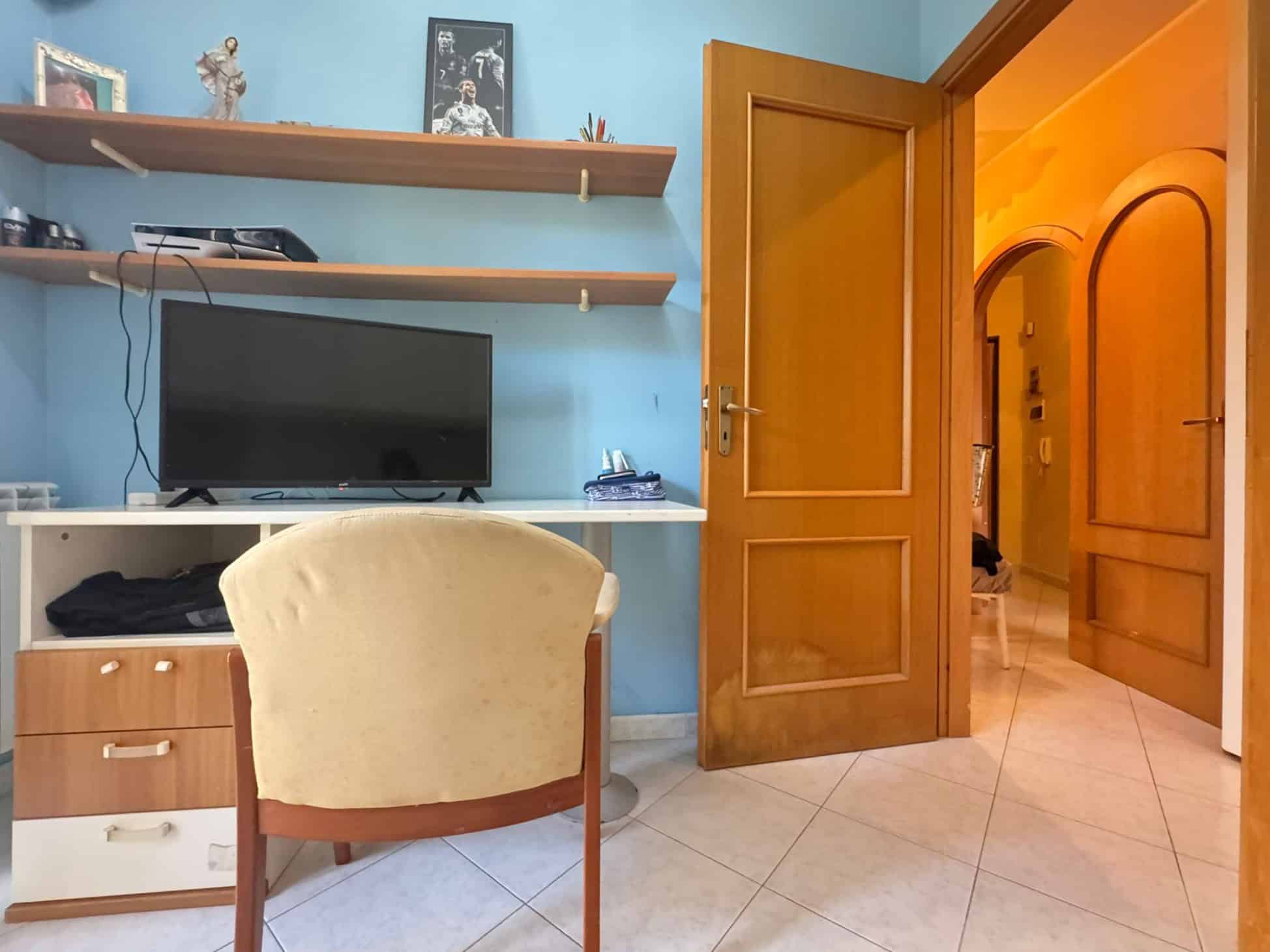 1. Ambiente domestico con scrivania, TV e scaffali in stile semplice, ideale per spazio studio o lavoro in casa.
