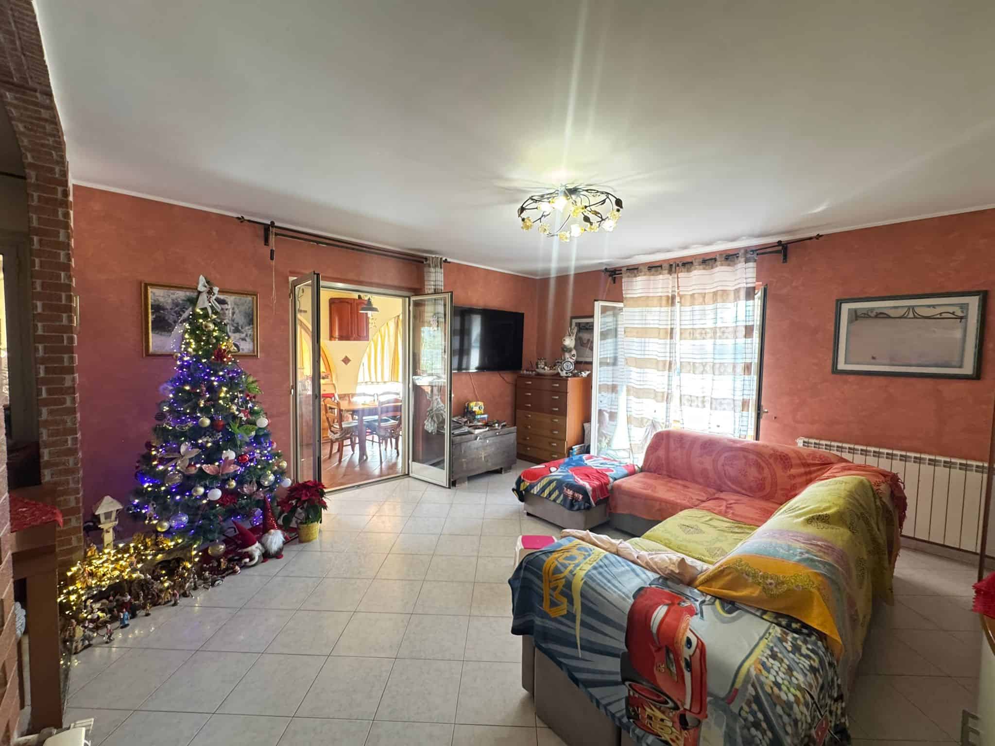 Albero di Natale decorato con luci e ornamenti nella soggiorno, ambiente luminoso e accogliente con divano, mobili in legno e velux che favoriscono l'ingresso di luce naturale, ideale per vendite immobiliari residenziali.