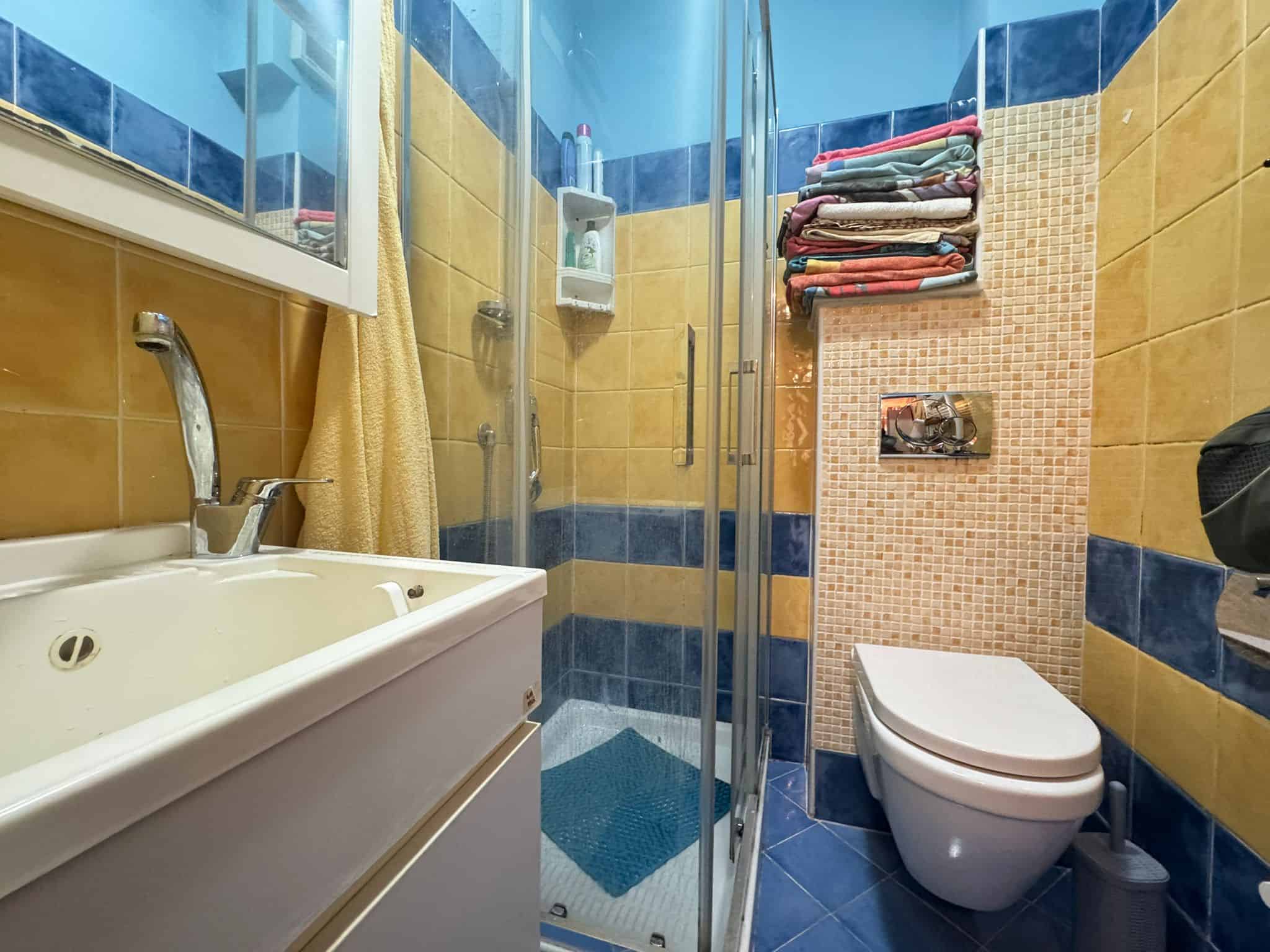 Vasca e doccia in bagno spazioso con piastrelle colorate, asciugamani e accessori, illuminato naturalmente, ideale per comfort e funzionalità, perfetto per appartamenti in vendita o affitto.