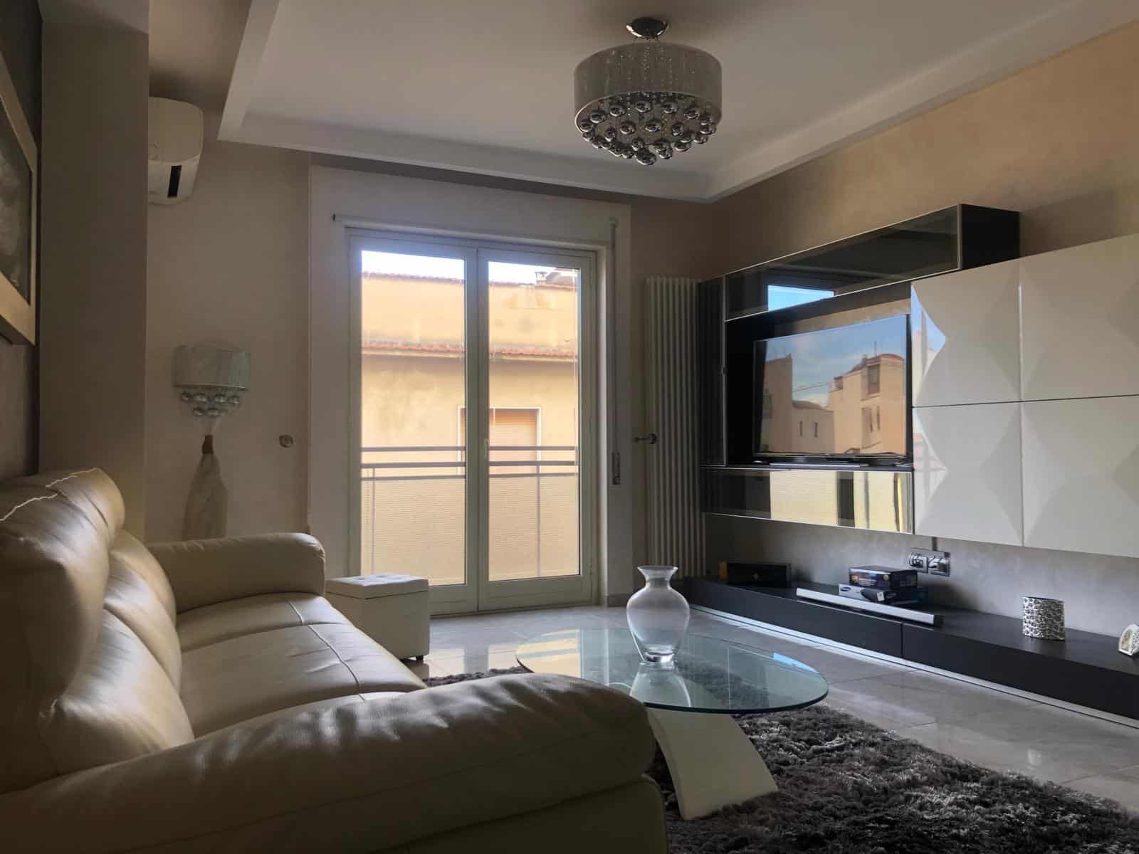 Appartamento moderno con soggiorno luminoso, divano beige, area Living con TV e parete attrezzata, grandi finestre con vista sulla città, arredi eleganti e stile contemporaneo.