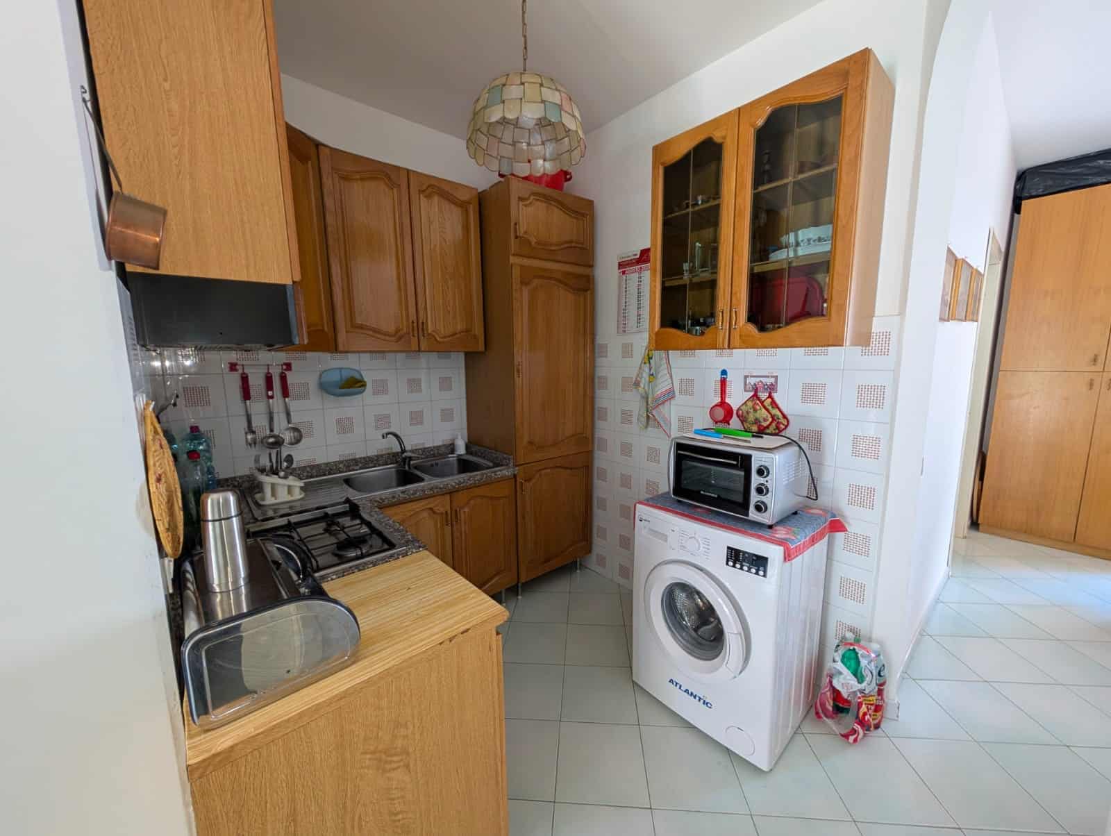 Lavanderia moderna con elettrodomestici e mobili in legno, cucina attrezzata con forno, microonde, lavatrice, spazio per stoccaggio e accessori domestici.