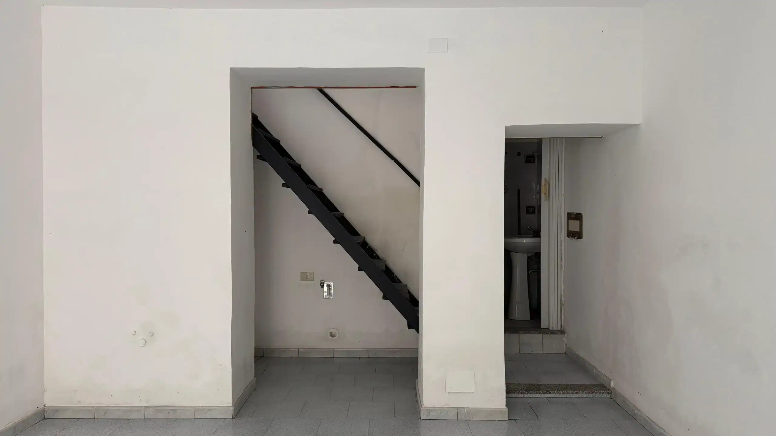 1. Ascensore interno di un appartamento moderno con scala nera, pareti bianche e pavimento in piastrelle, pronto per l'arredamento.